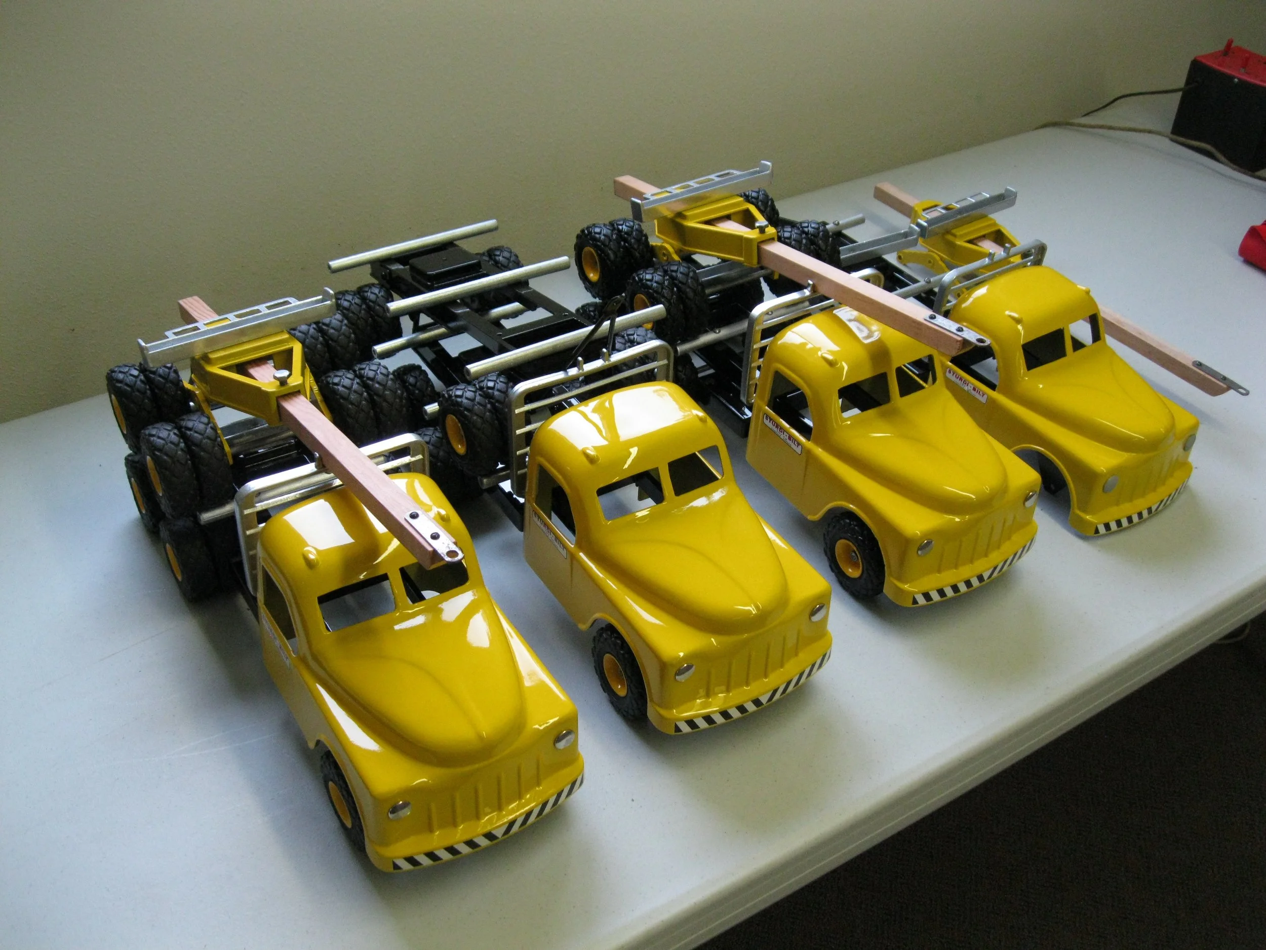 Three toy cars with yellow bodies and black wheels, connected to makeshift trailers with tires, on a white table.