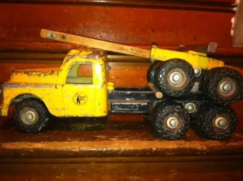 Yellow toy tow truck with a ladder attached, placed on a wooden surface.