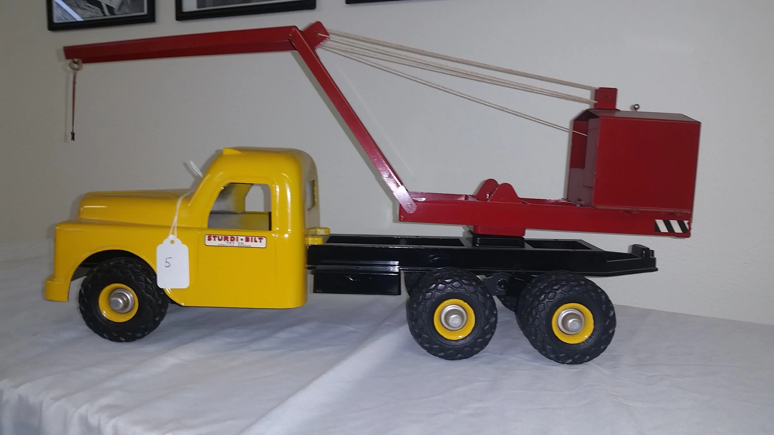 A yellow toy tow truck with a red boom and black base, displayed on a white surface.