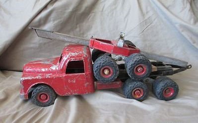 Red toy tow truck with six black wheels on a beige fabric surface.