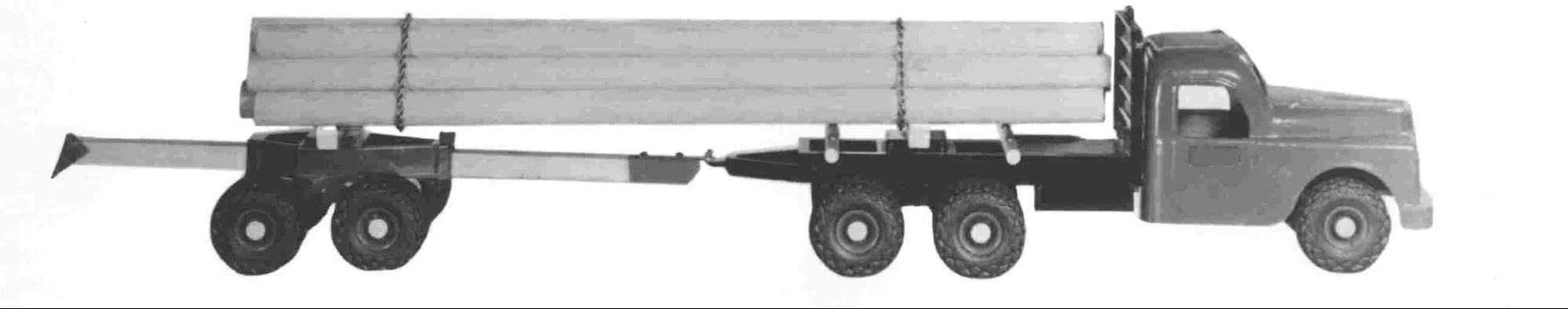 Black and white image of a large utility truck carrying long pipes on its bed.