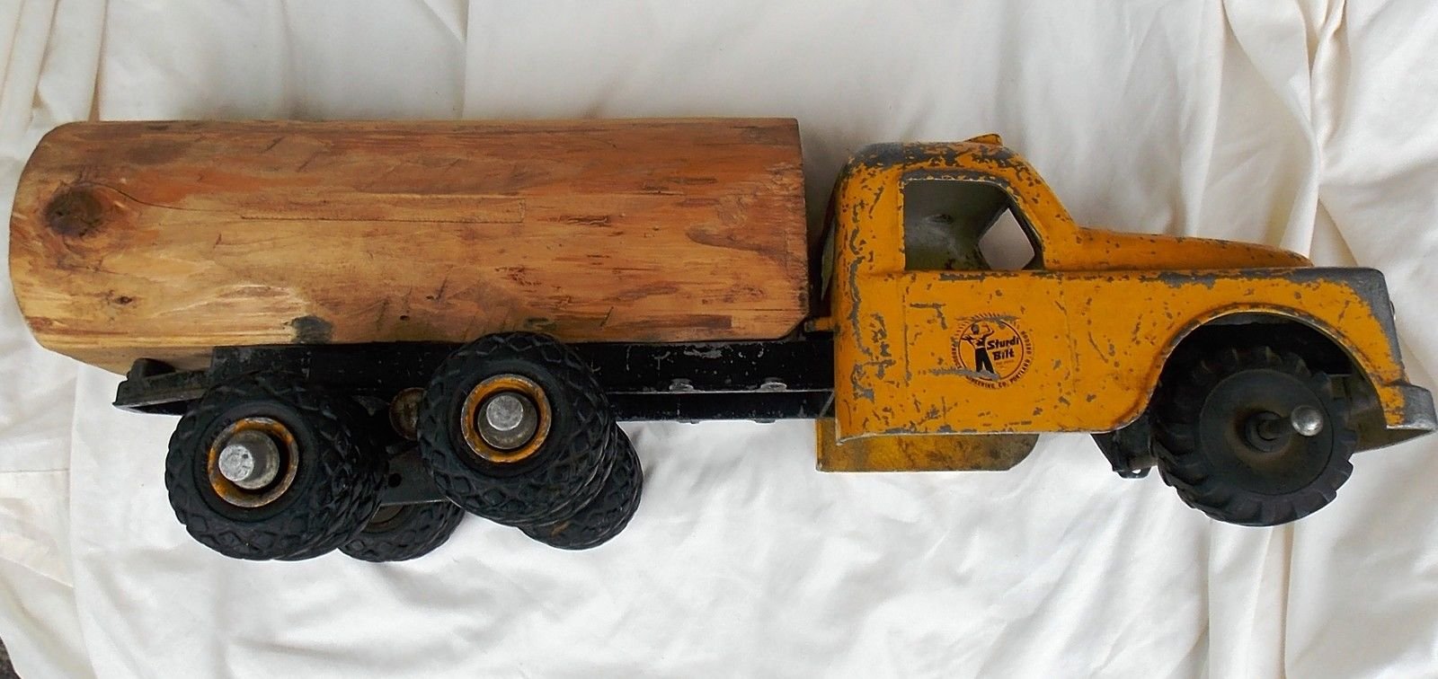 Vintage toy truck with a yellow cab, black chassis, and a wooden bed, positioned on a white fabric background.