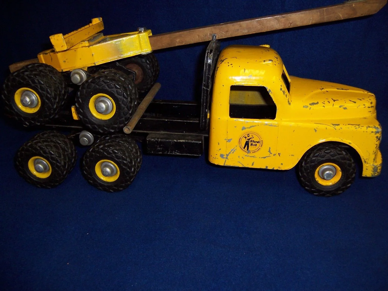 A vintage yellow toy truck with black wheels, chipped paint, and a logo on the door, placed on a dark blue surface.