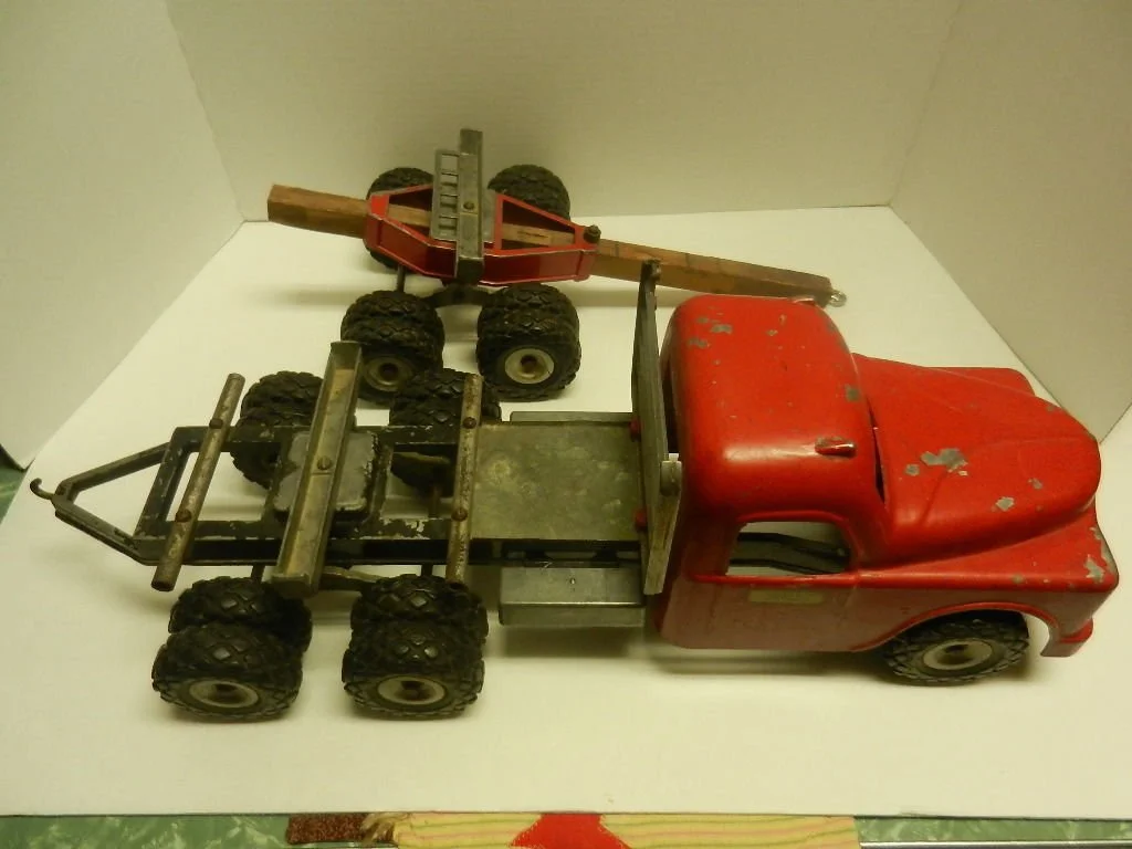 Vintage red toy truck with an empty flatbed and a smaller red and black toy vehicle on top, placed on a white surface against a plain background.