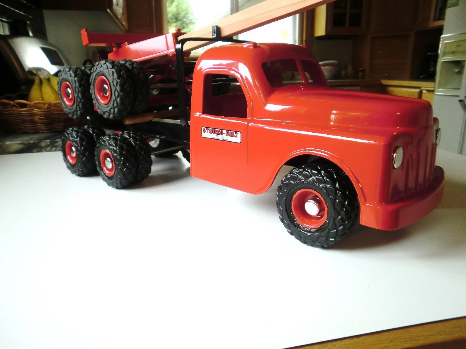 A red toy truck with large black tires with red rims, positioned on a white surface in a kitchen.