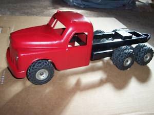 Red toy truck with a black flatbed, placed on a beige surface.