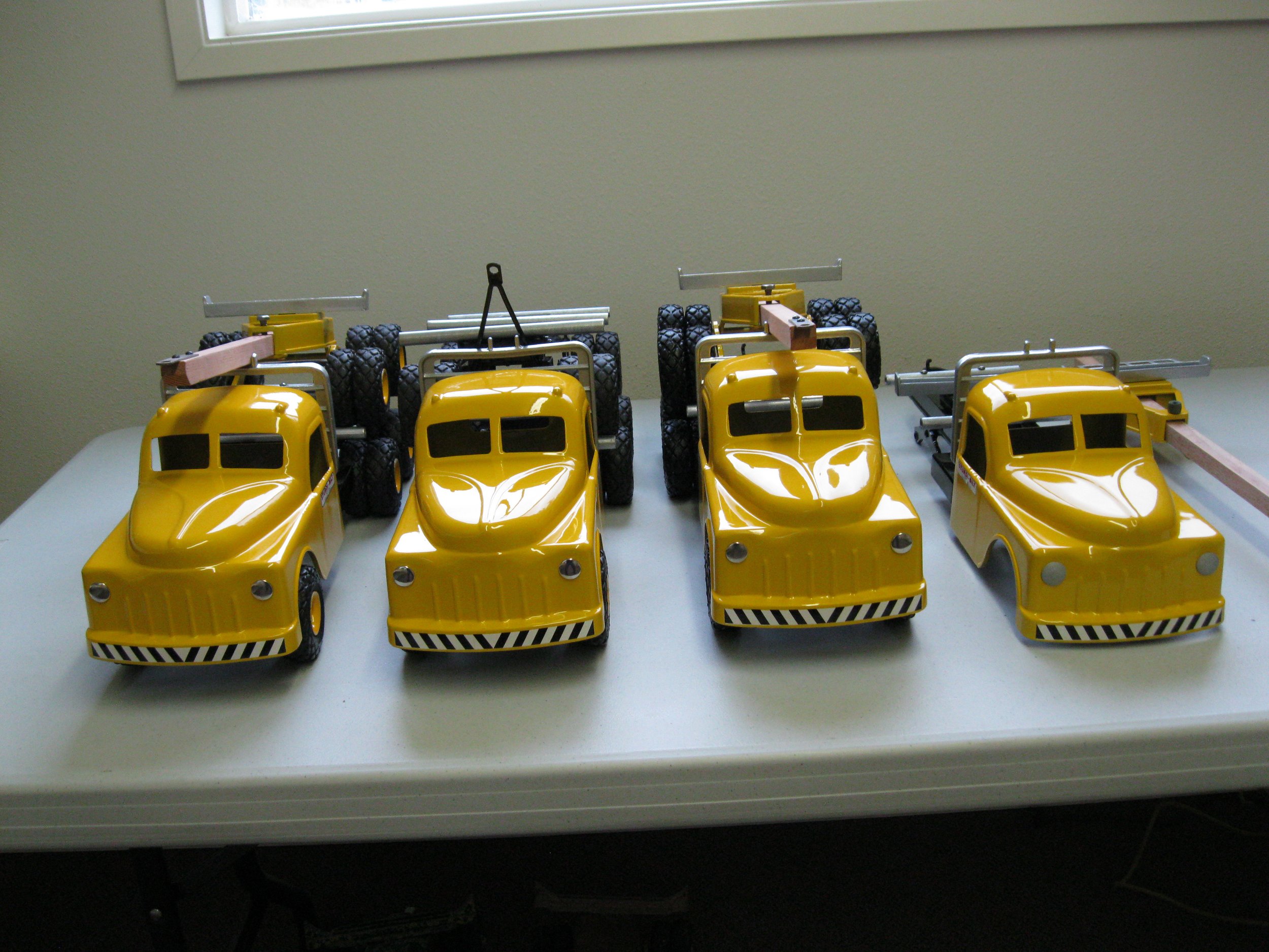 Four yellow toy tow trucks with black tires lined up on a white table.