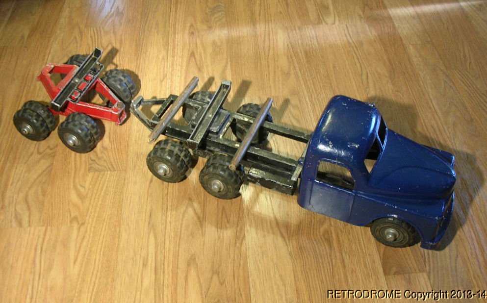 A vintage blue toy fire truck with a red and black toy wrecking ball attachment on a wooden floor.
