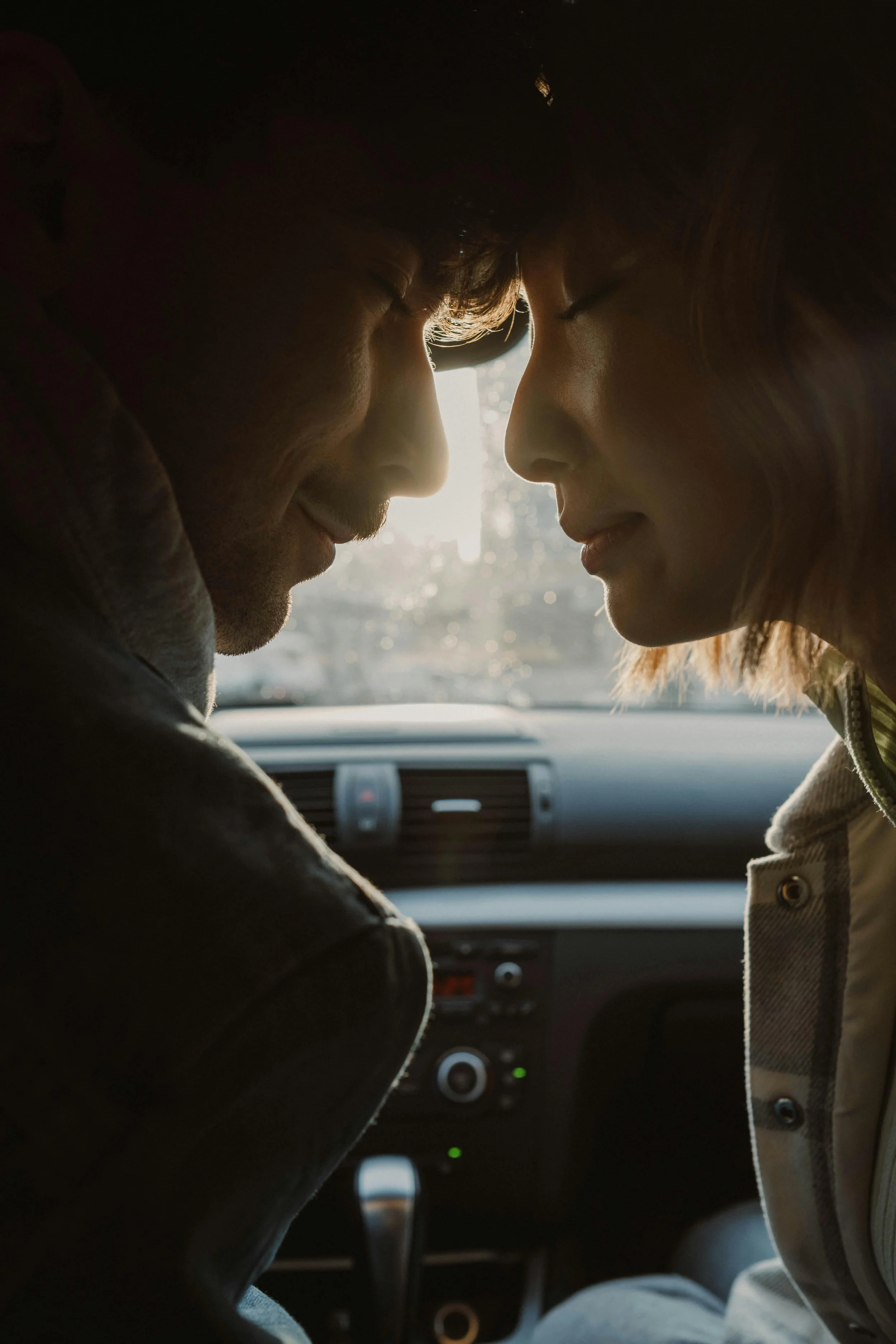 a man and a women in a car touches heads together with their eyes closed
