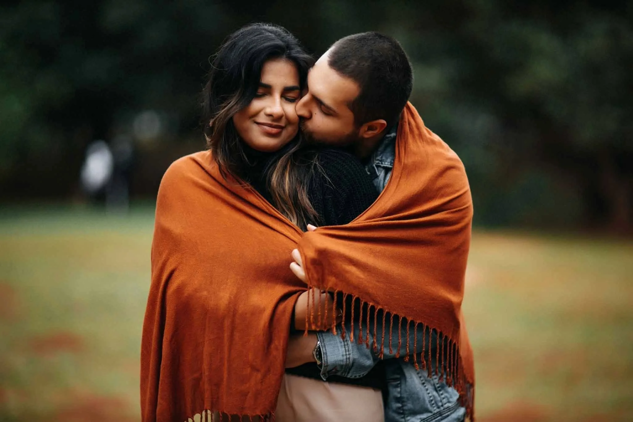 a man and women embracing outside in a large scarf
