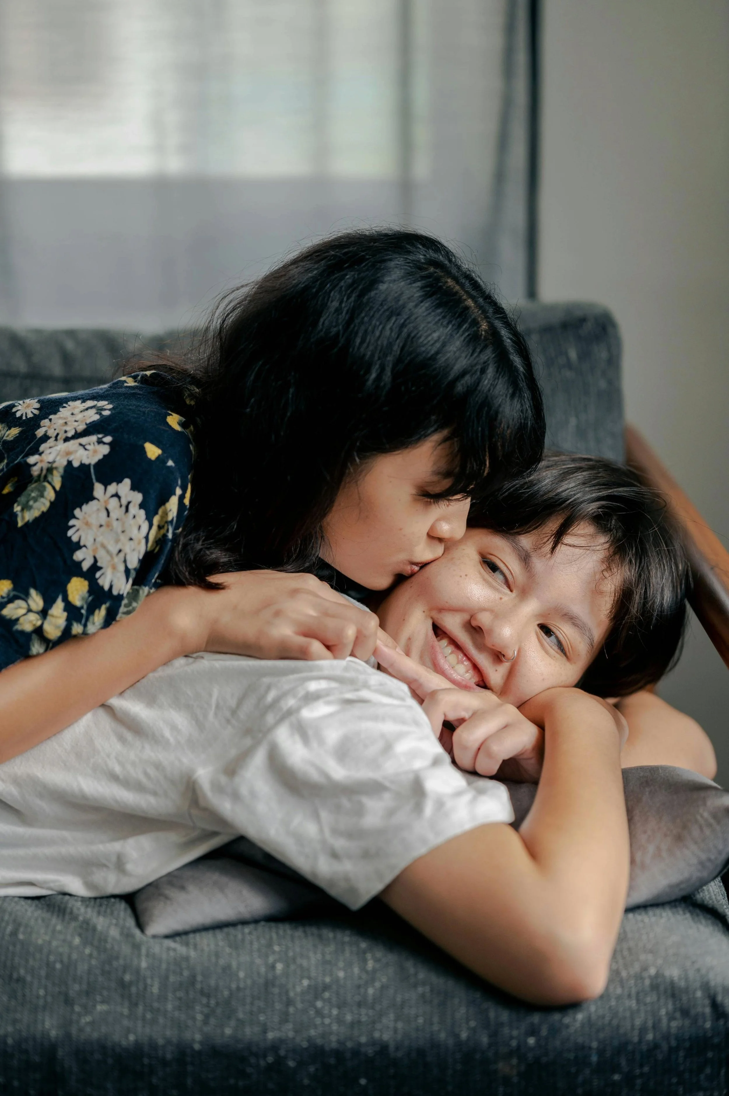 two women laying on a couch on top of each other where the one on top is kissing the other women's cheek
