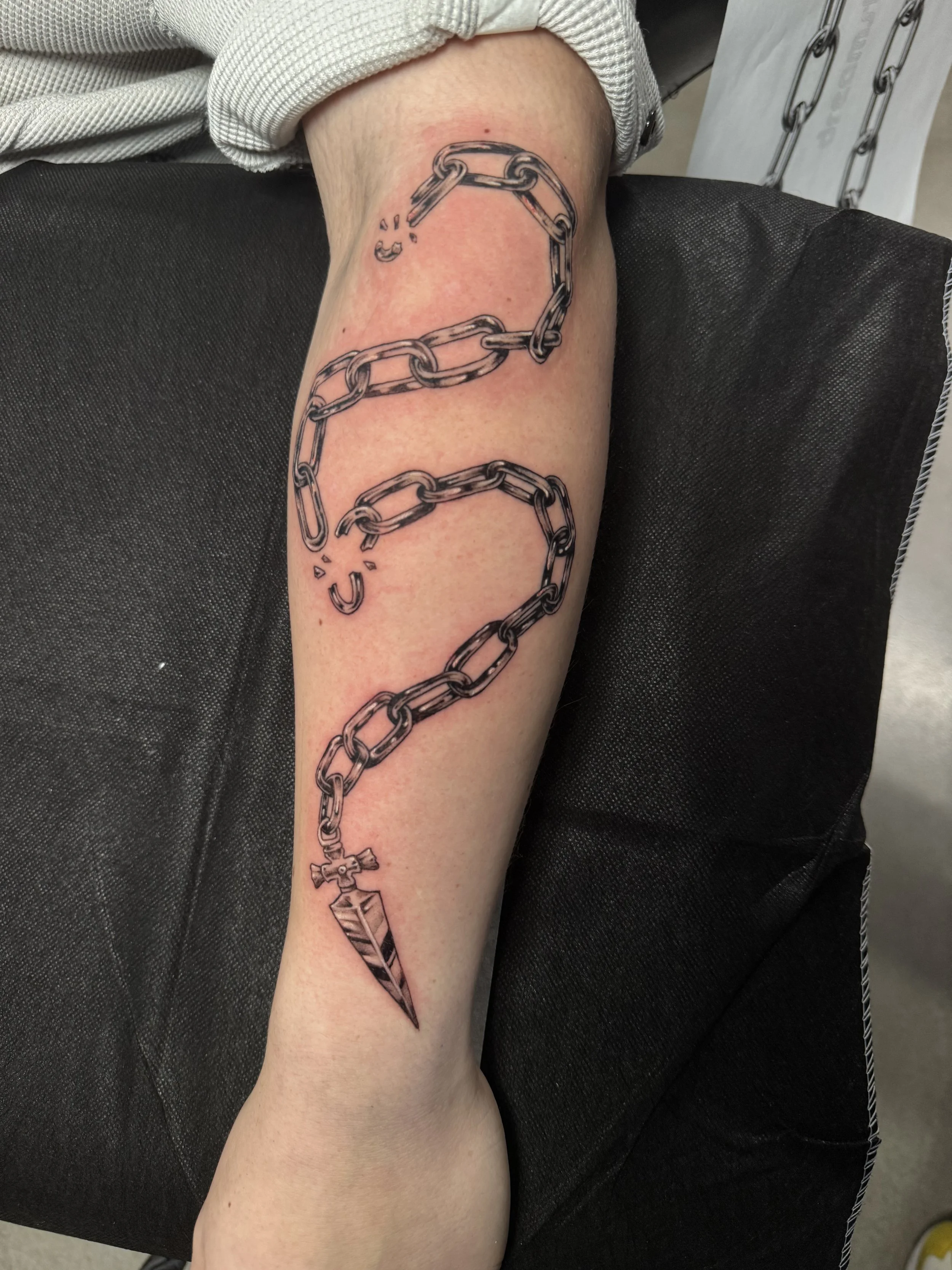 Tattoo of a broken chain with a spearhead end on a person's forearm.