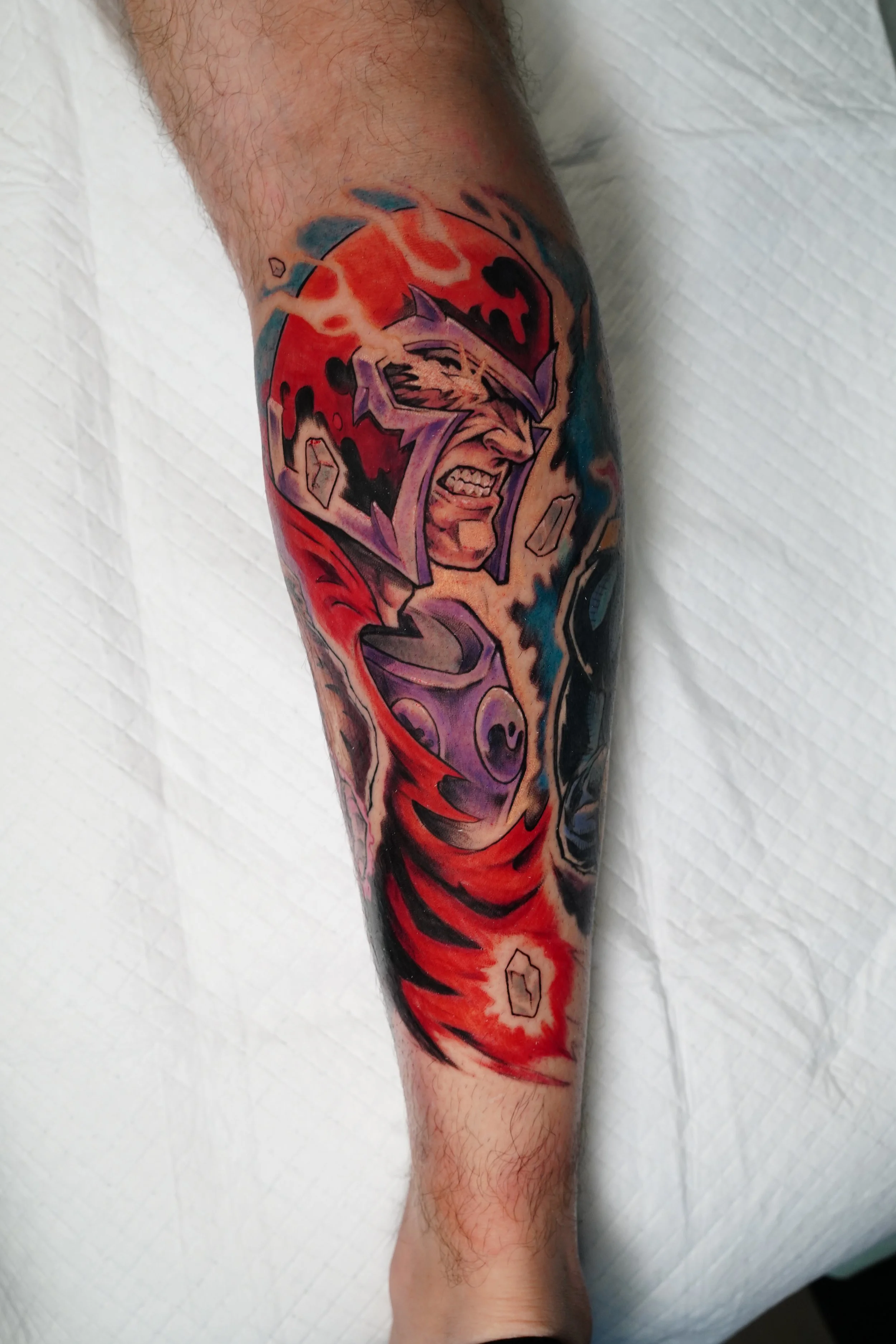 Colorful tattoo of a comic-style character with a fierce expression, wearing a purple helmet and red cape, with a fiery background and abstract elements.