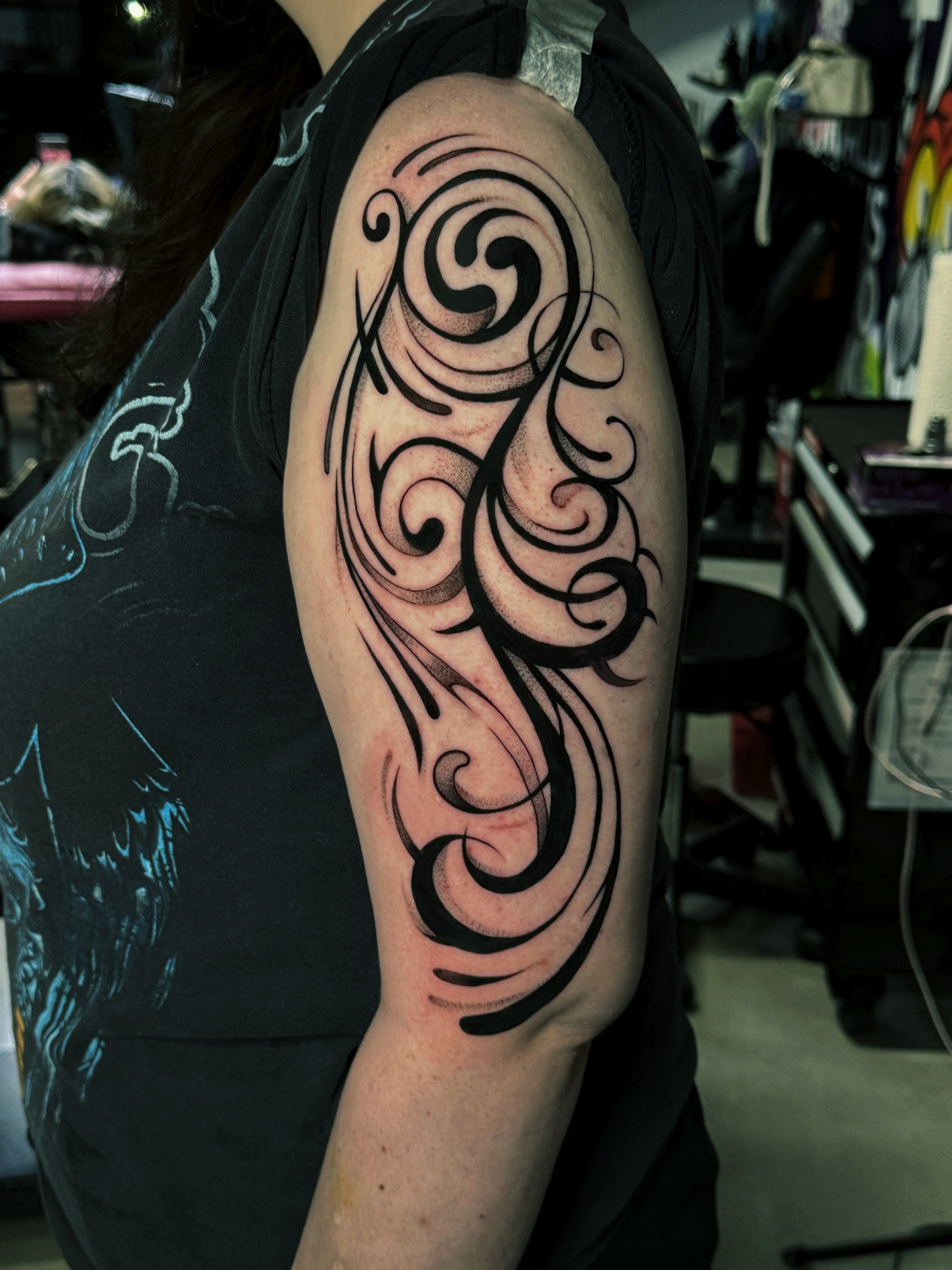 Tattoo of swirling black abstract lines on upper arm.