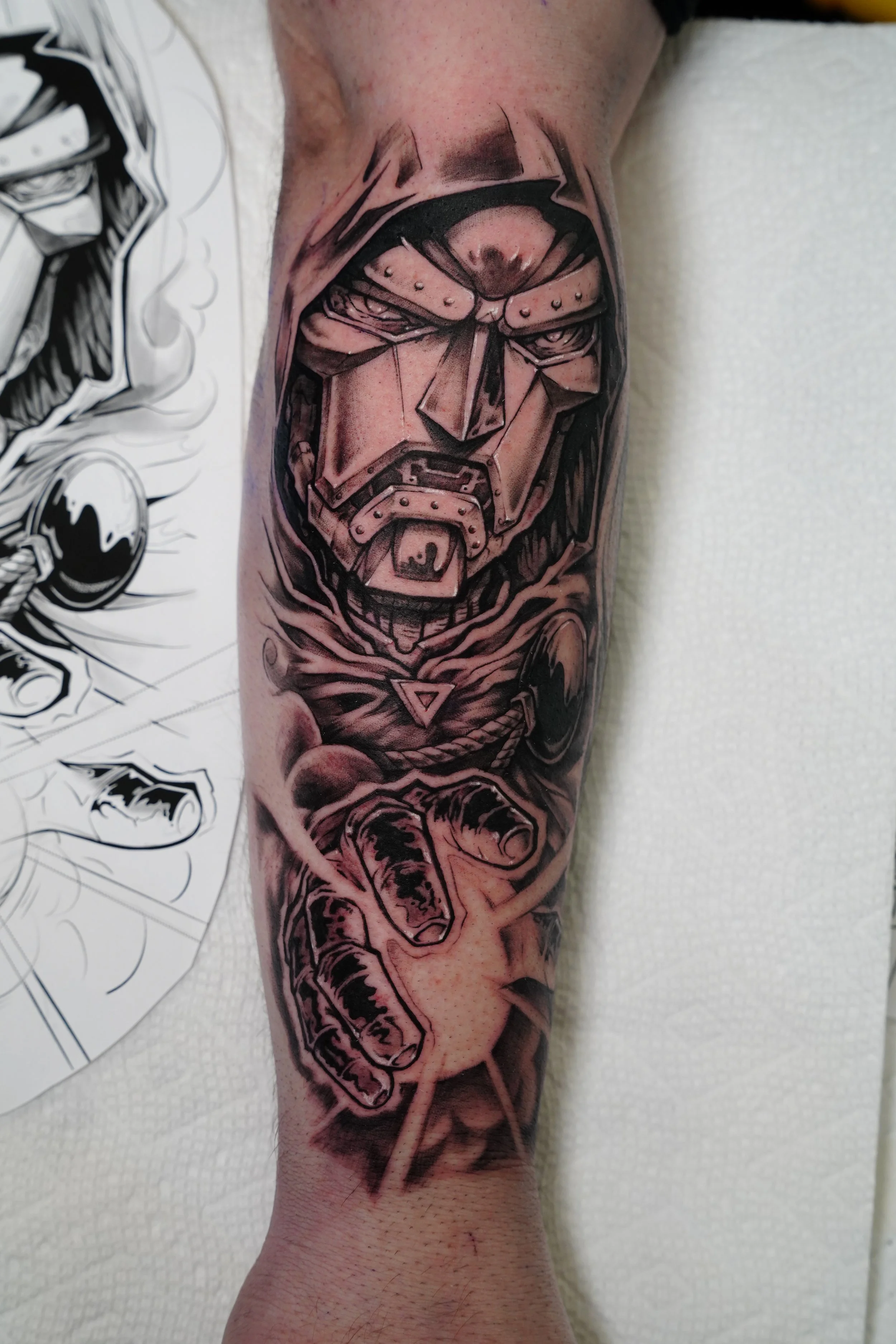 Tattoo of a robotic or armored face with a stern expression and a pointing hand, detailed with dark shading and bold outlines.