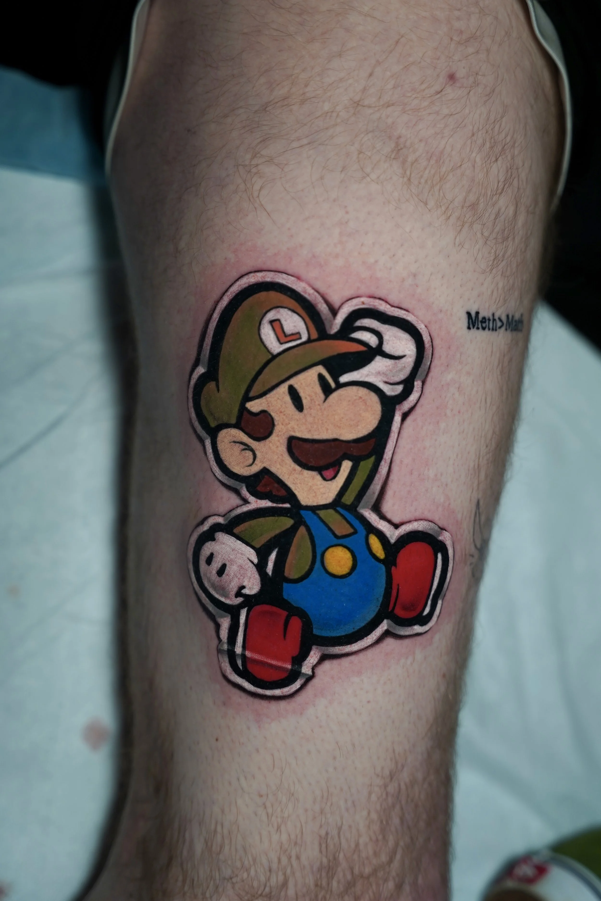 Colorful tattoo of Luigi from Super Mario on a person's thigh.