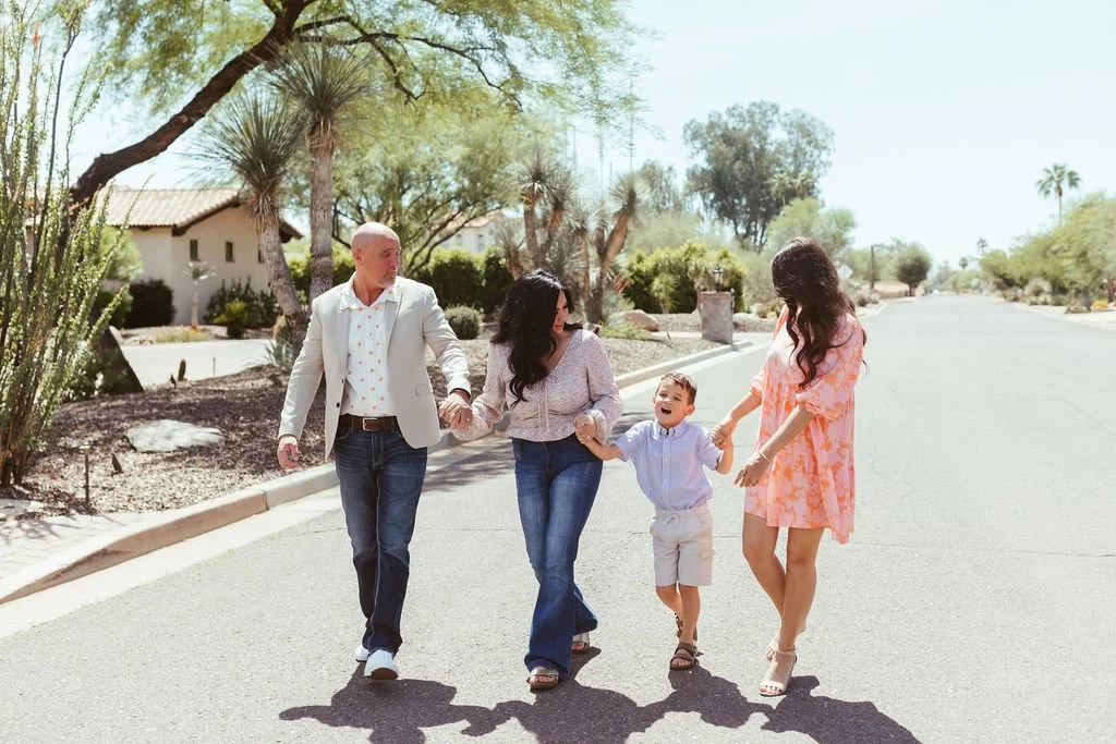 A family of four walking hand in hand down a suburban street, smiling and enjoying a sunny day.