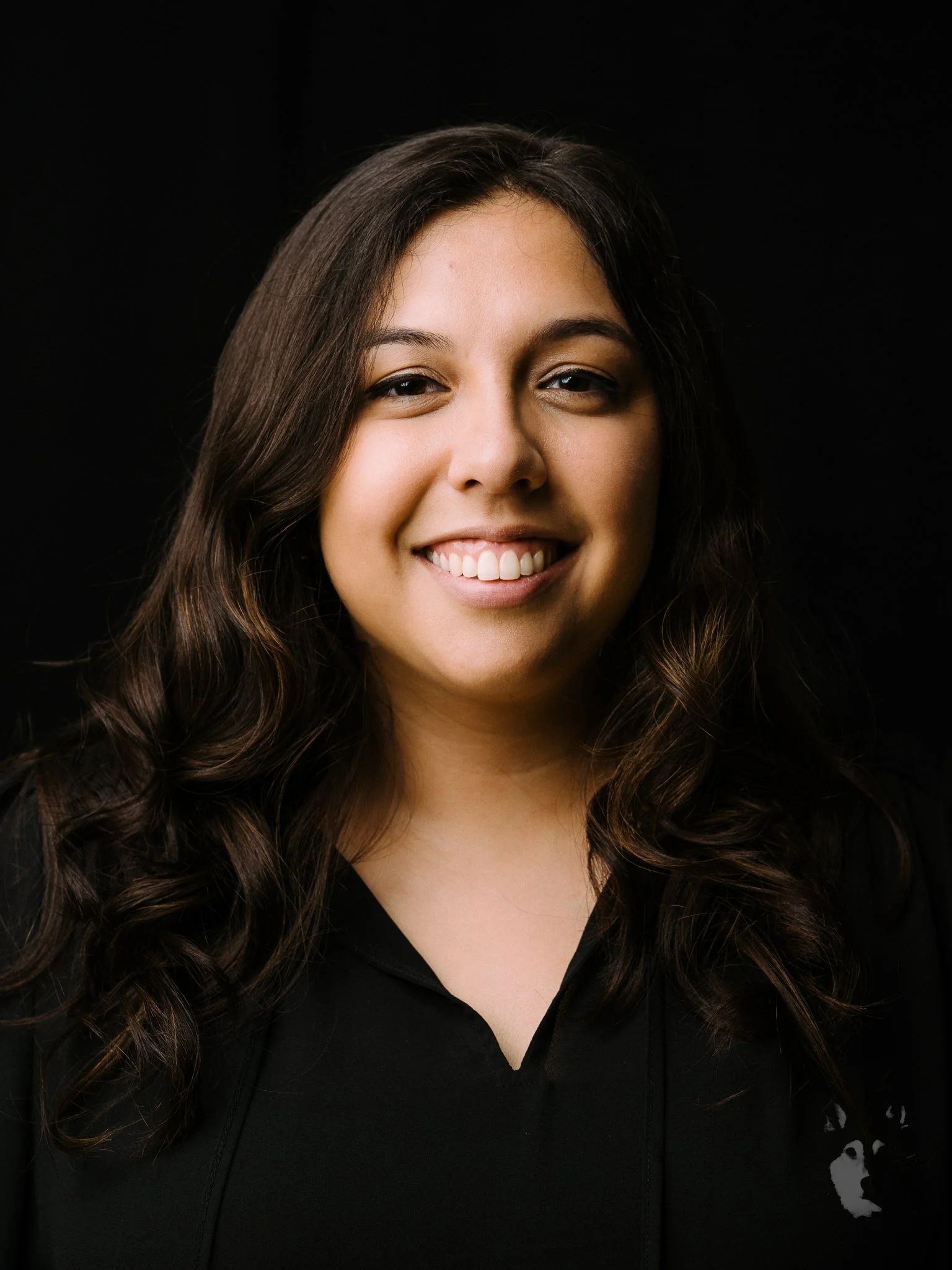 A young woman with wavy dark brown hair smiling against a black background.