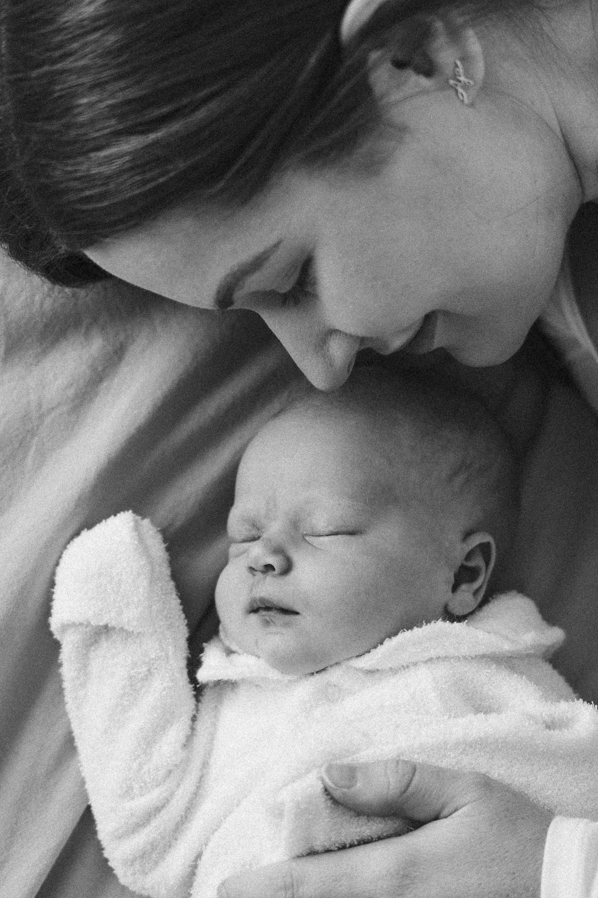 A woman holding a sleeping newborn baby, nuzzling her nose to the baby's forehead, in black and white.