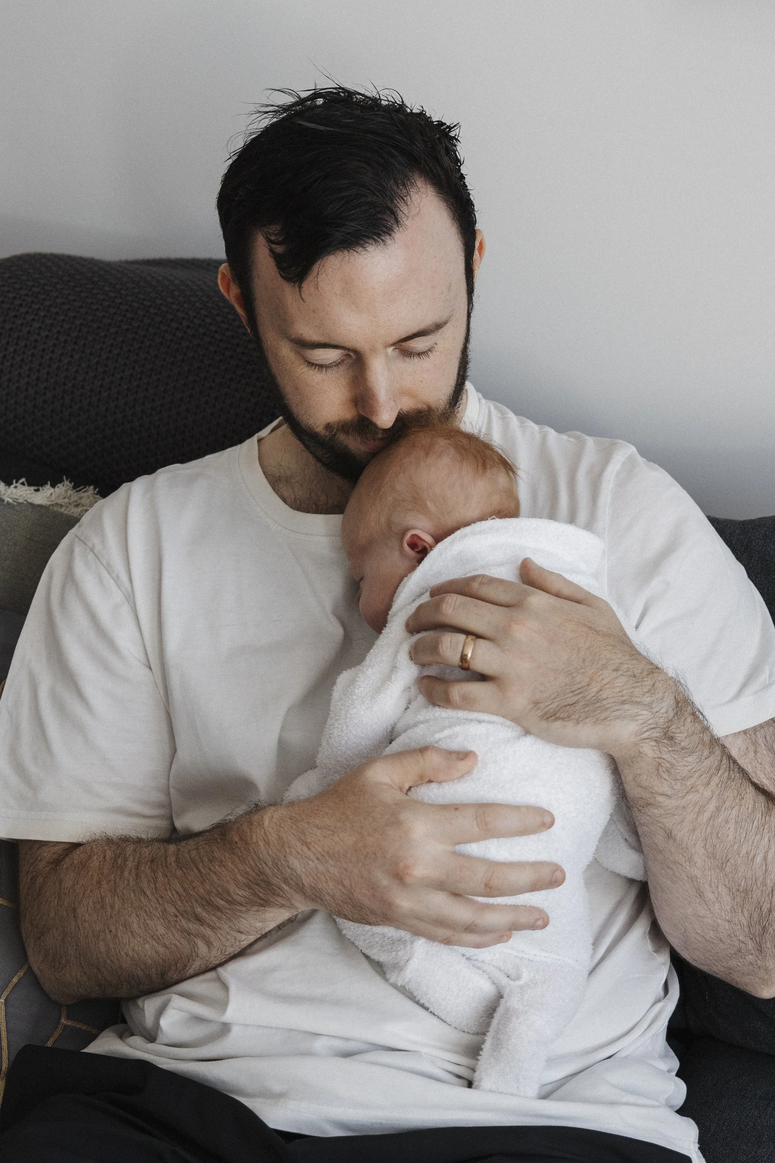 A man is holding a baby wrapped in a white towel, gently cradling it against his chest.