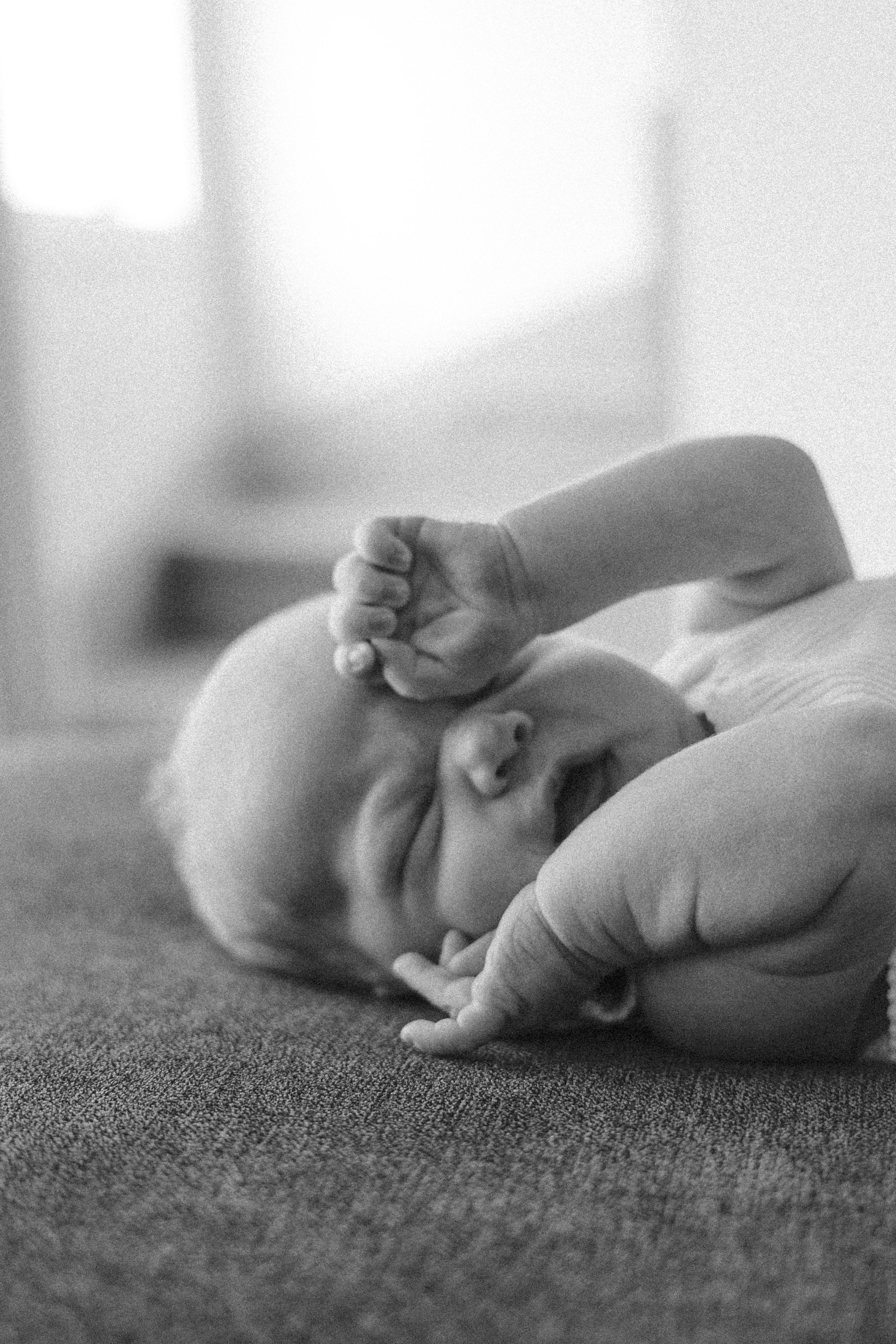 A baby lying on a soft surface, crying or upset, with an adult's hand gently holding the baby's head and arm.