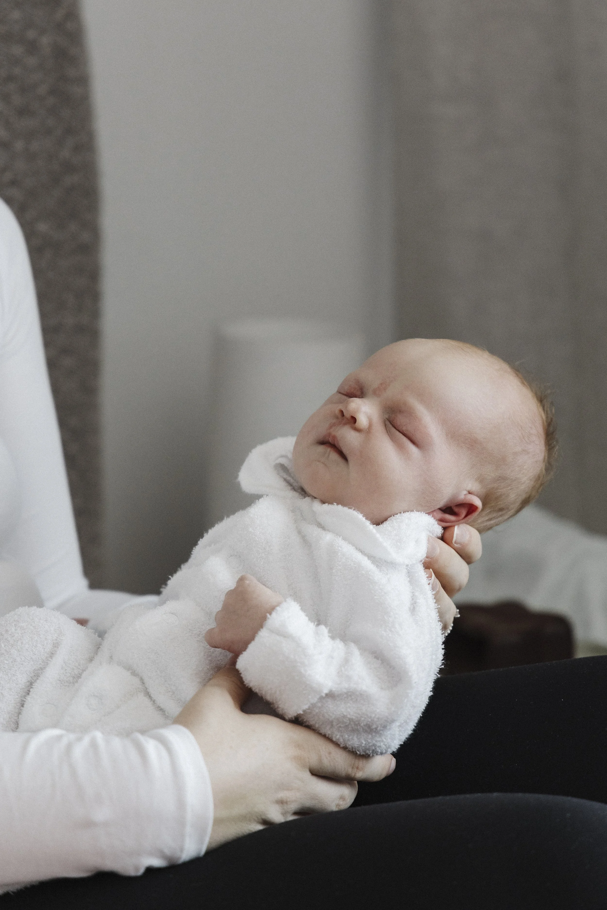 Close-up of a sleeping baby in a white hoodie being held by an adult.