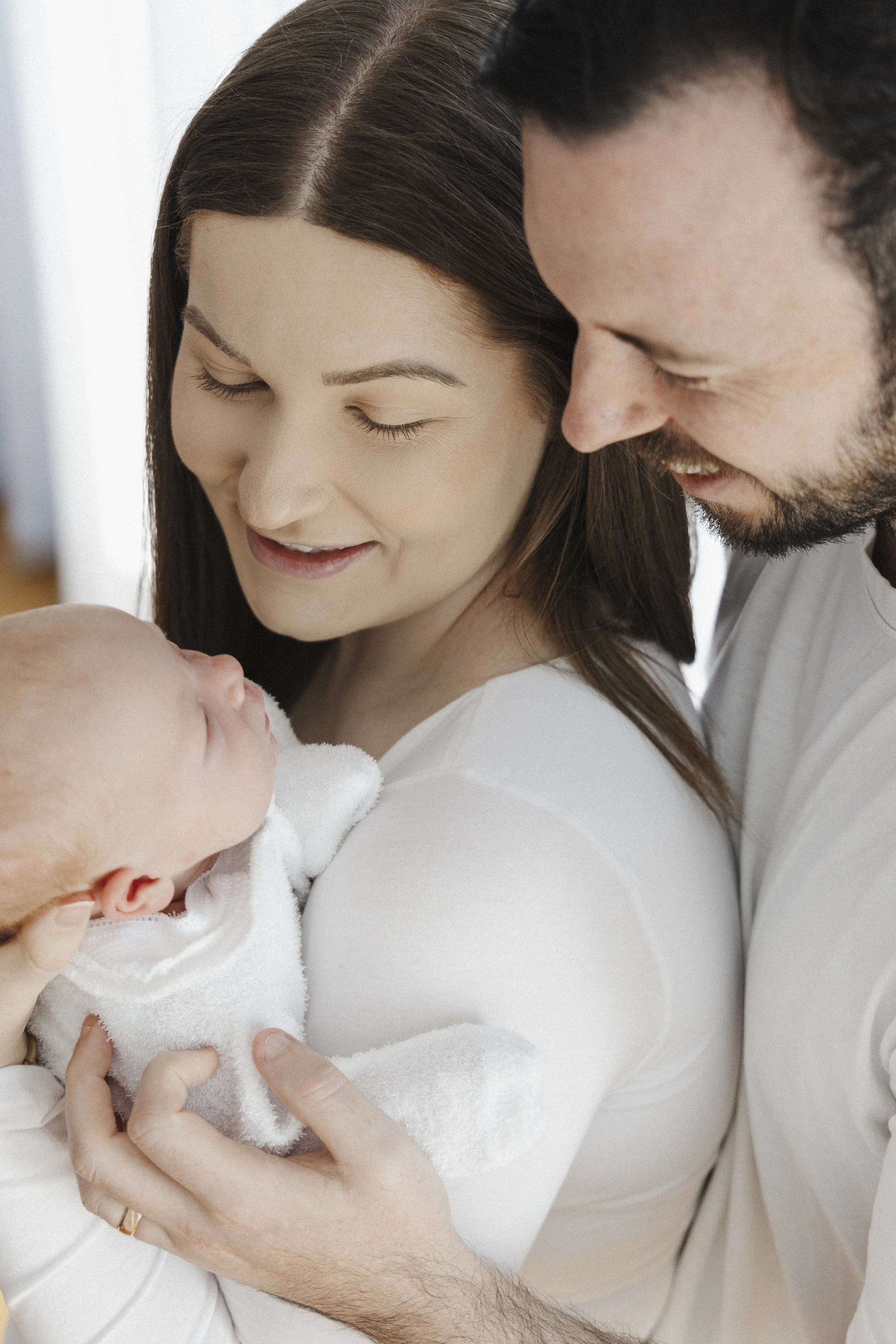 A happy couple holding their newborn baby indoors, close to each other.