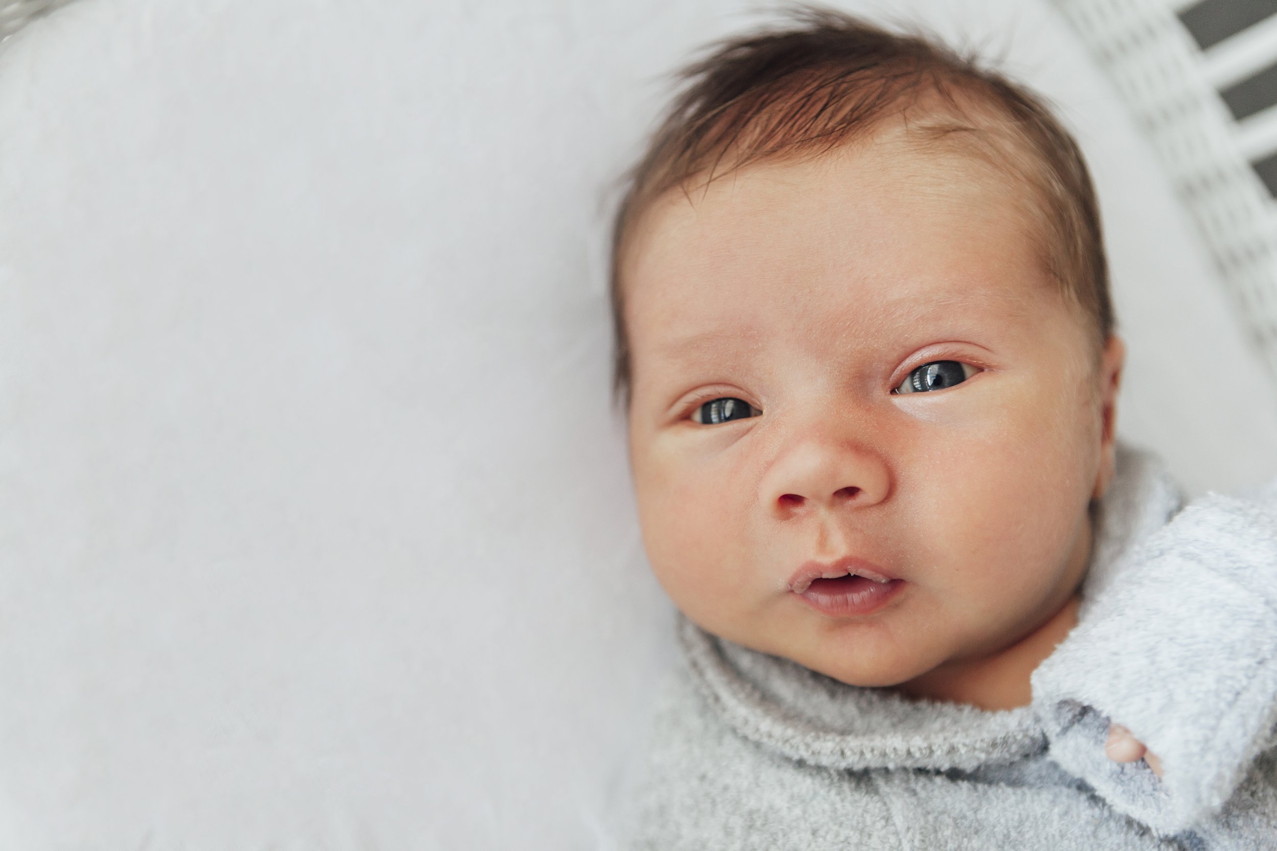 Close-up of a newborn baby with blue eyes lying on a white surface.