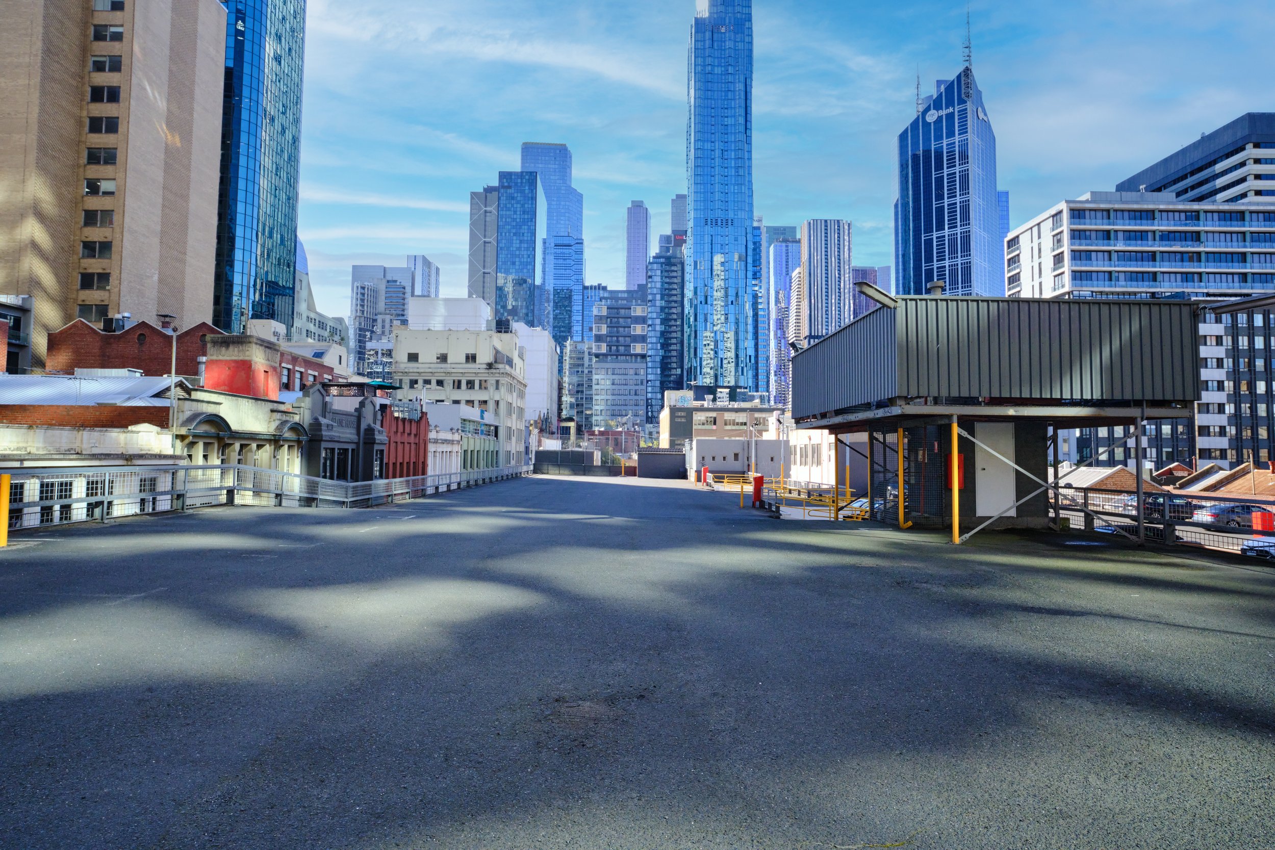 Empty rooftop parking lot in a city with tall modern glass skyscrapers in the background.
