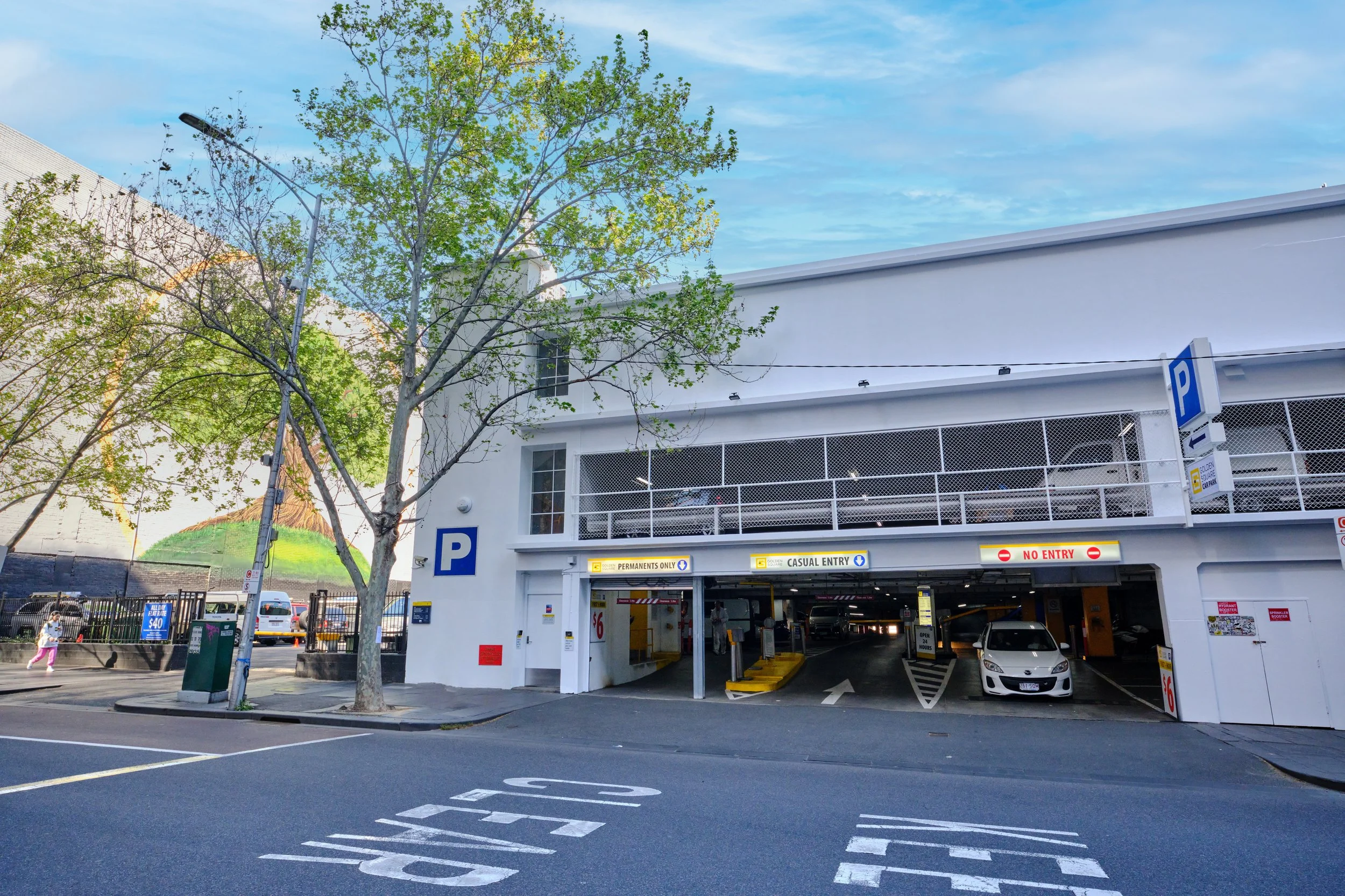 Multi-level parking garage entrance with signs for 'Peripherals Only', 'Casual Entry', and 'No Entry'; cars parked inside, trees in front, clear blue sky overhead.