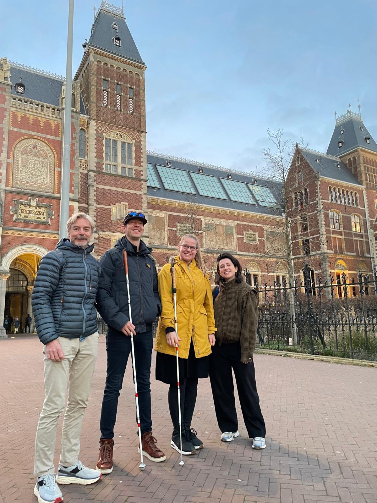 Vier mensen poseren voor het Rijksmuseum, van wie twee met een blindenstok.