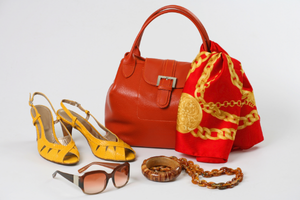 A flat lay of fashion accessories featuring a bold red handbag, patterned scarf, yellow heels, brown sunglasses, and jewelry, highlighting vibrant color coordination for a stylish ensemble.