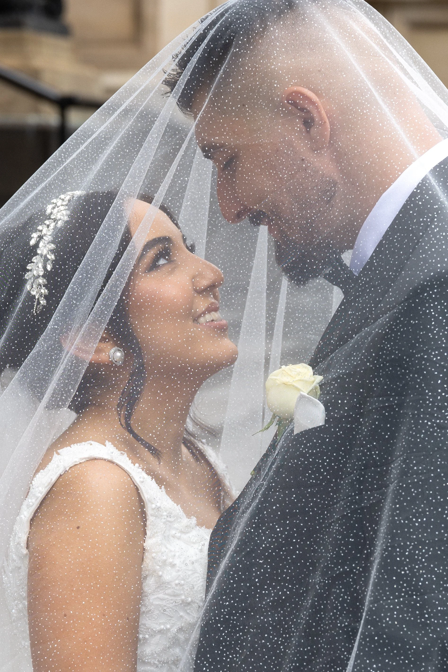 A bride and groom under a wedding veil looking into each other's eyes during their wedding ceremony.