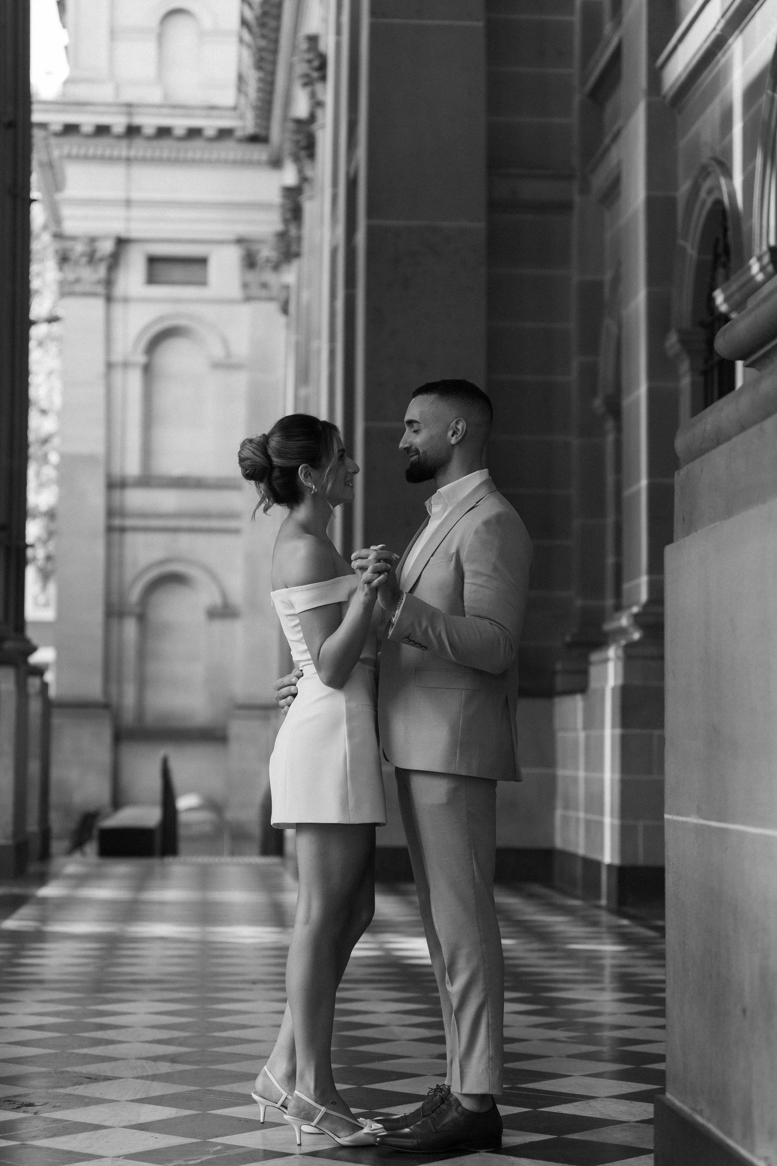 A couple dancing closely inside a historic building with ornate architecture, black and white photo.