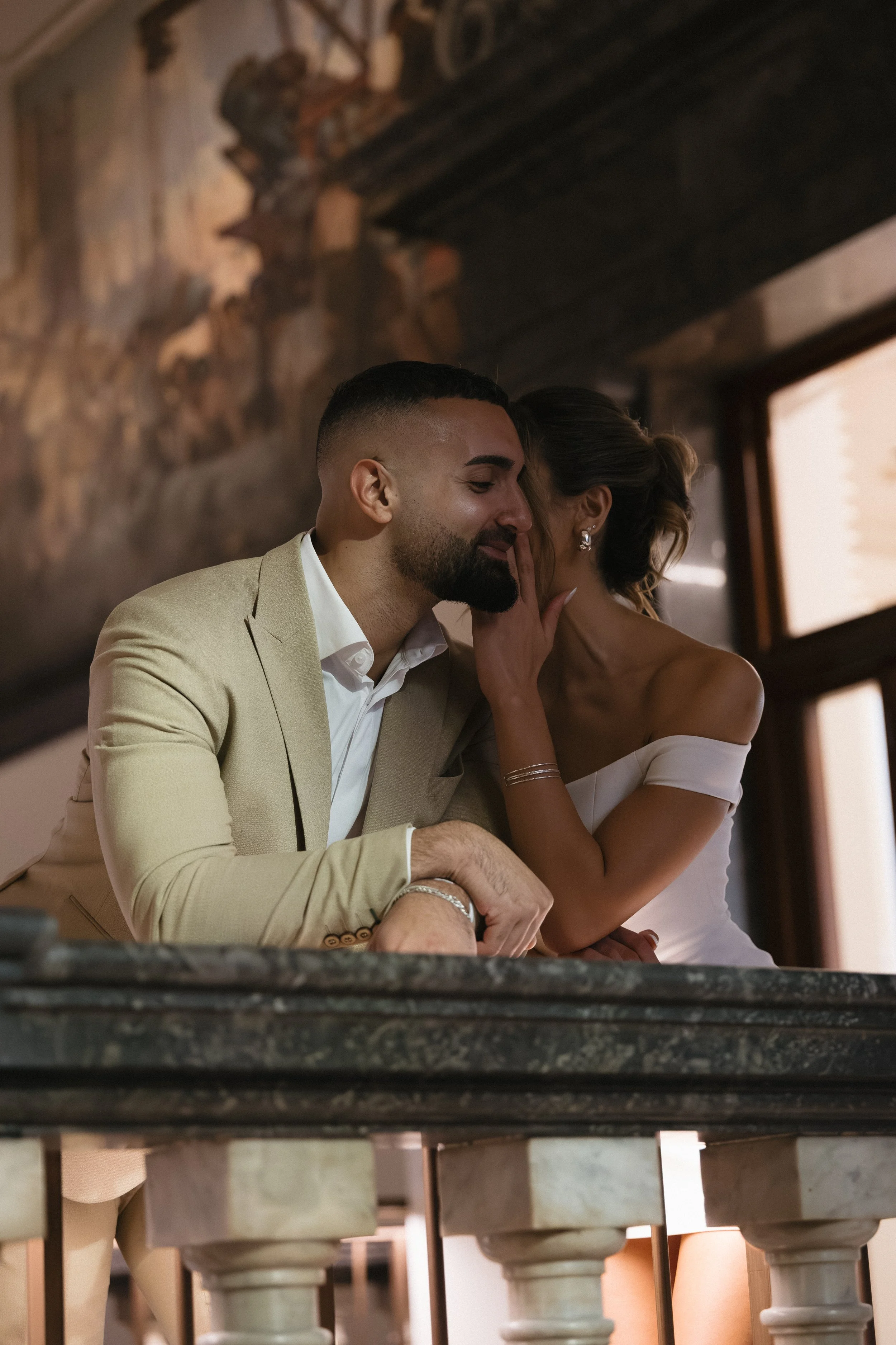 A couple whispering or sharing a secret in a romantic embrace, with a rustic interior background.