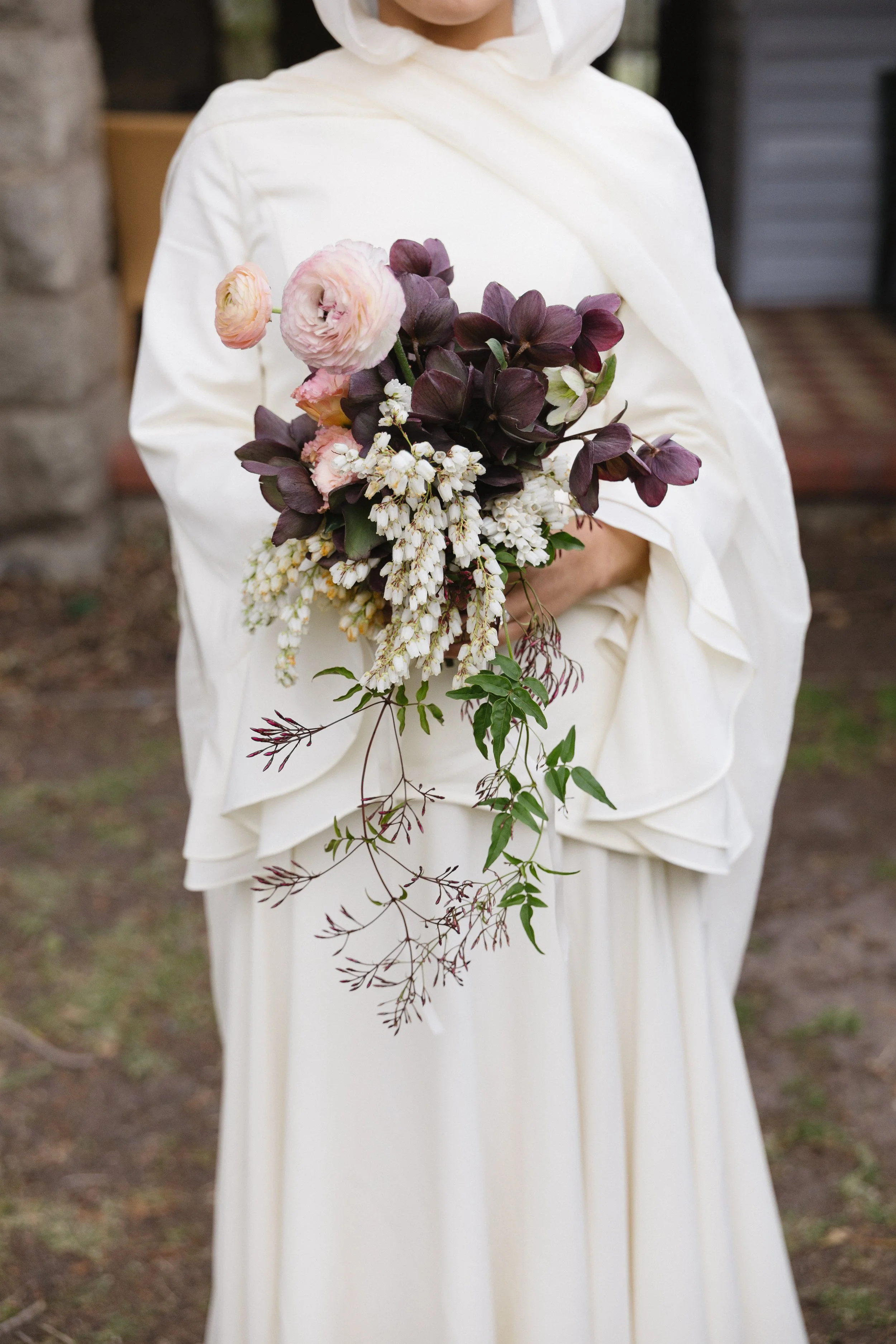 Person in a white dress holding a bouquet of pink, purple, white, and green flowers