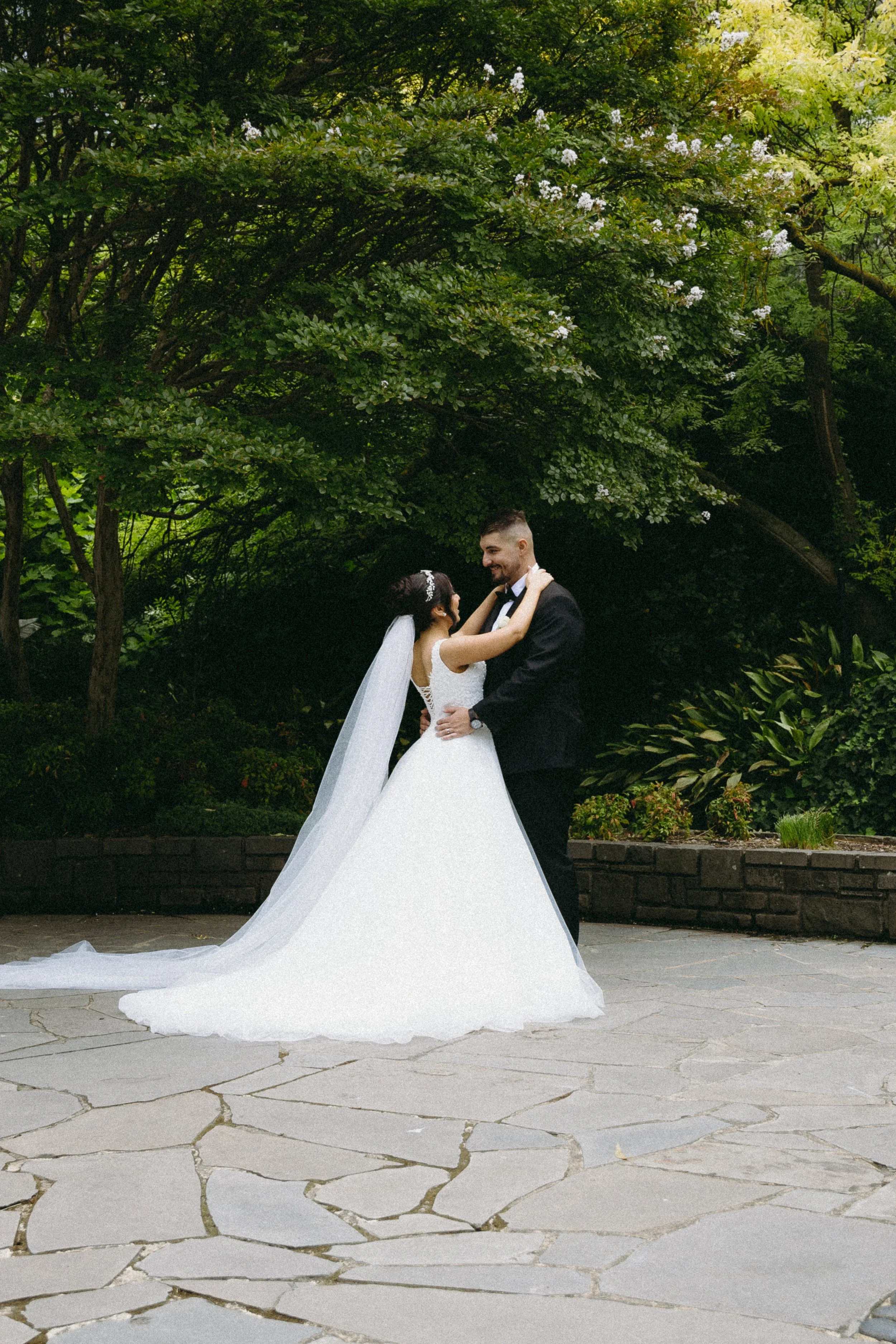 A bride and groom dancing outdoors on a stone pathway surrounded by greenery.