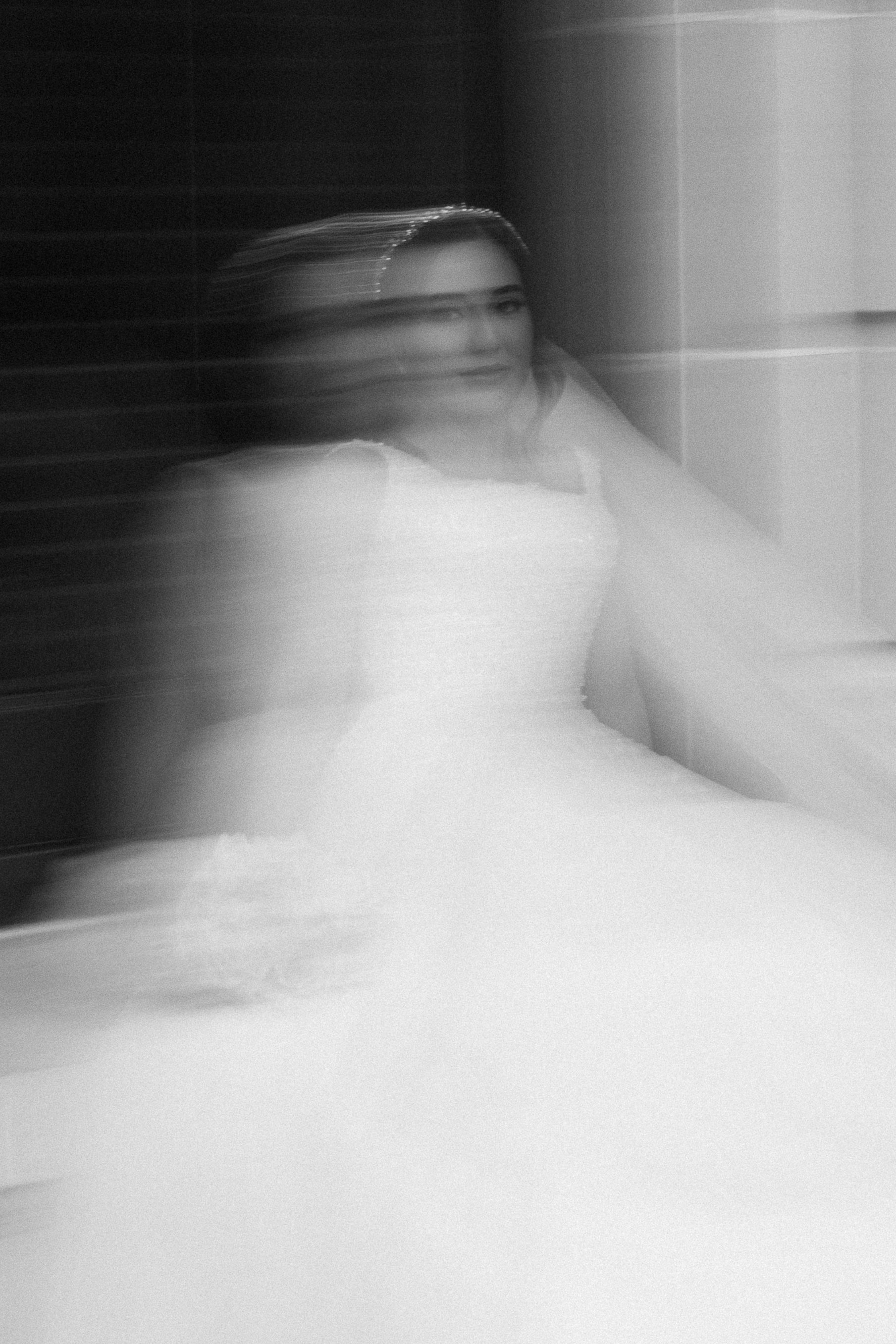 Black and white photo of a woman in a wedding dress sitting indoors with blurry motion effect.
