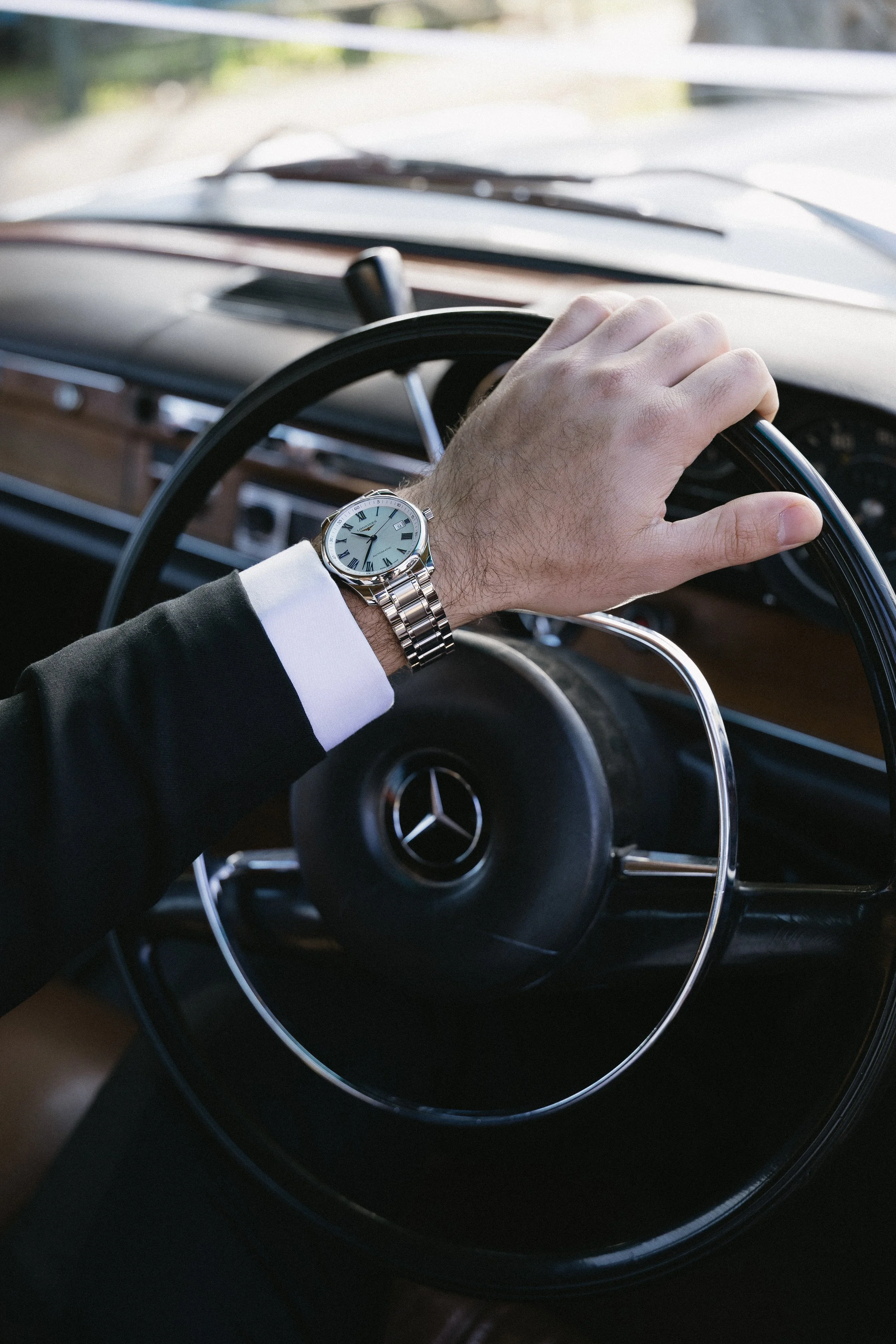 A person with a silver wristwatch driving a classic Mercedes-Benz car.