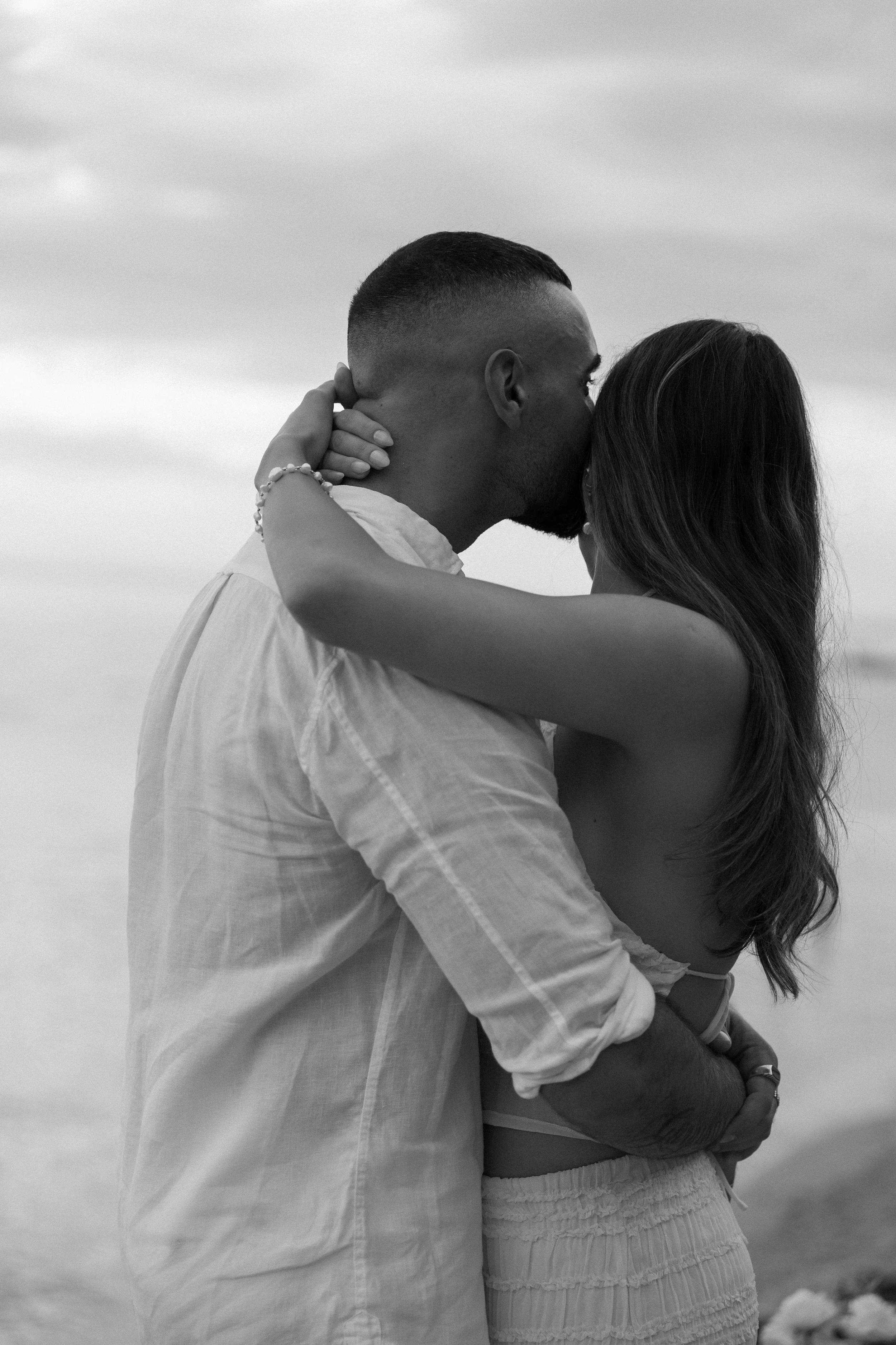 A black and white photo of a couple embracing and kissing on the beach.