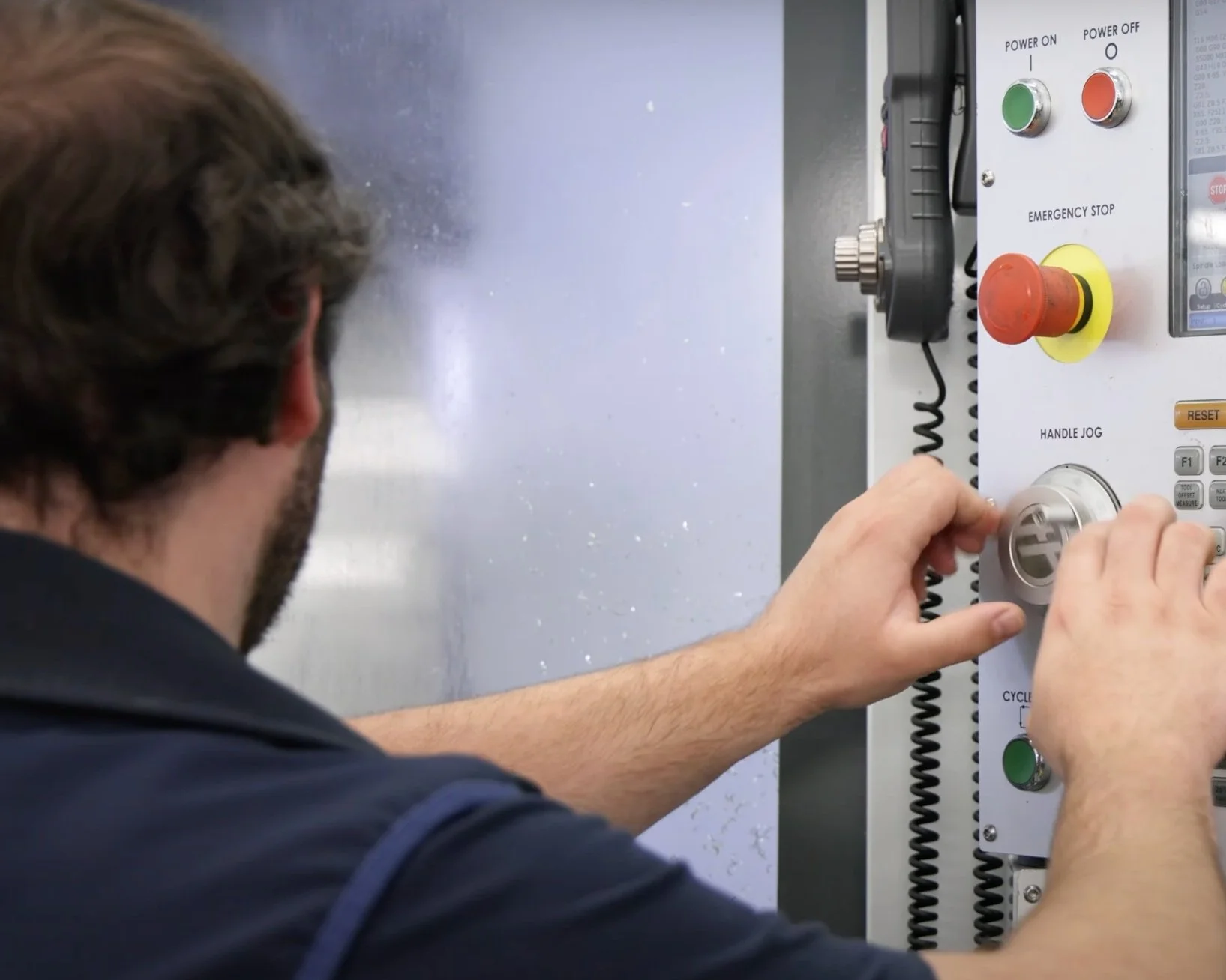 A male engineer facing towards a machine, turning a dial on a control panel.