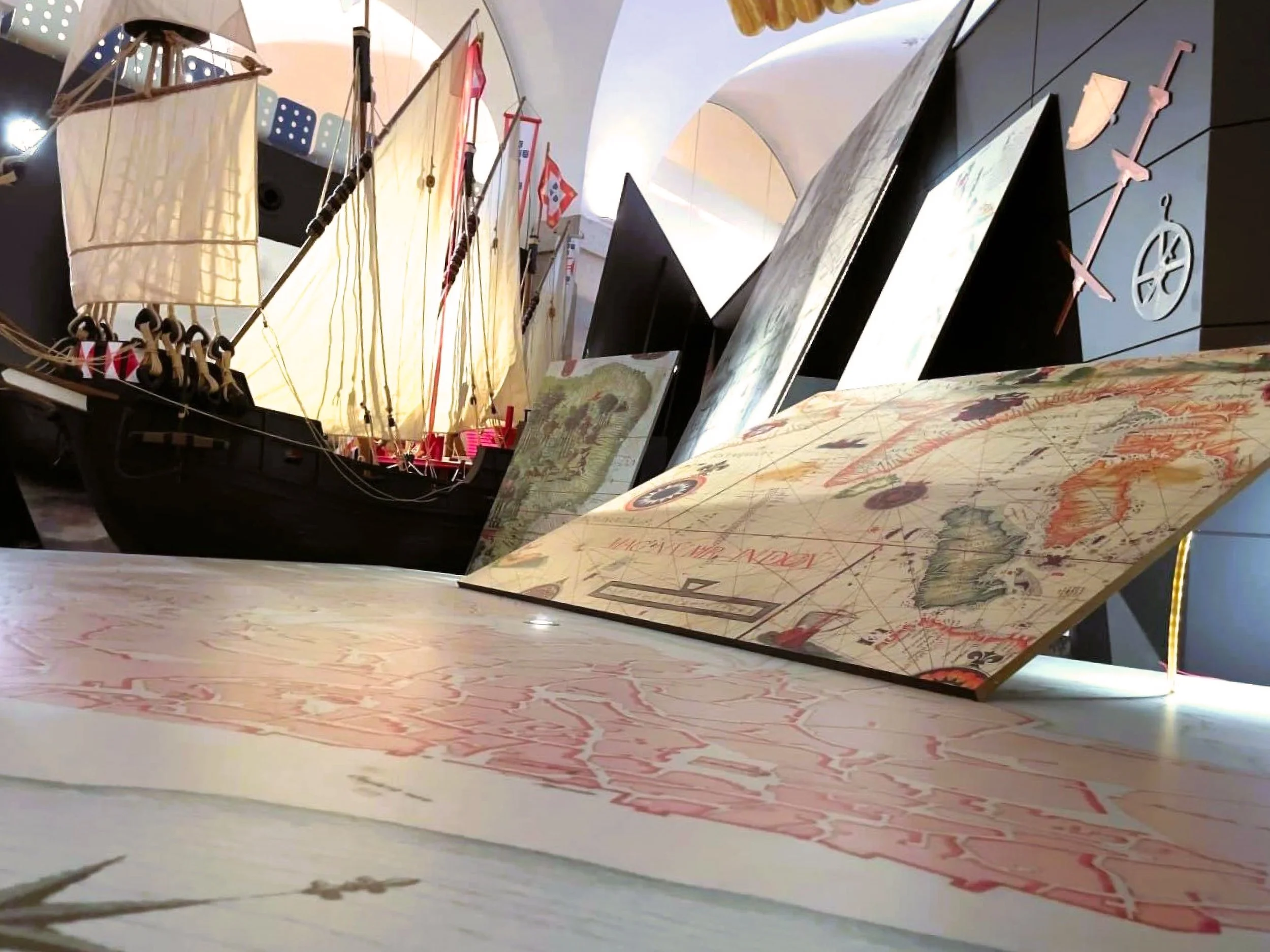 ADDESIGN ® Display of a detailed model ship with sails, navigational maps, and maritime-themed decorations in a museum or exhibit setting.