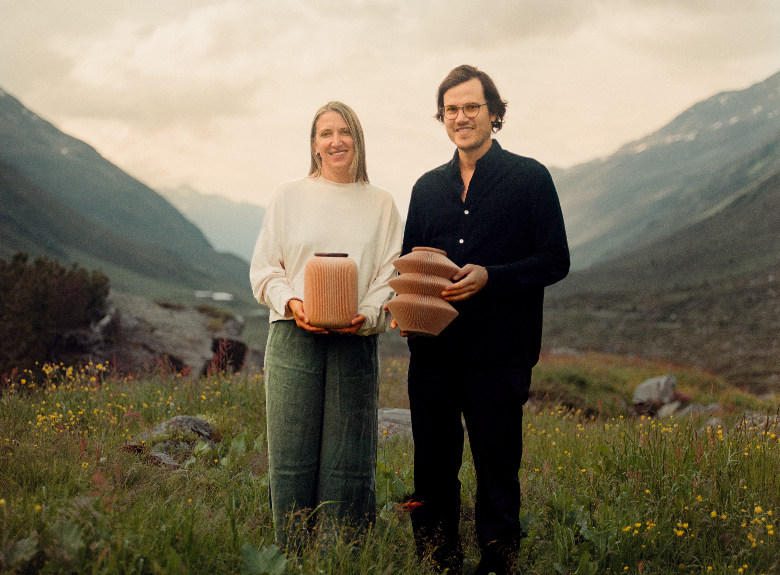 Katharina und Sebastian, Gründer von Farvel, mit zwei Urnen in einer Berglandschaft