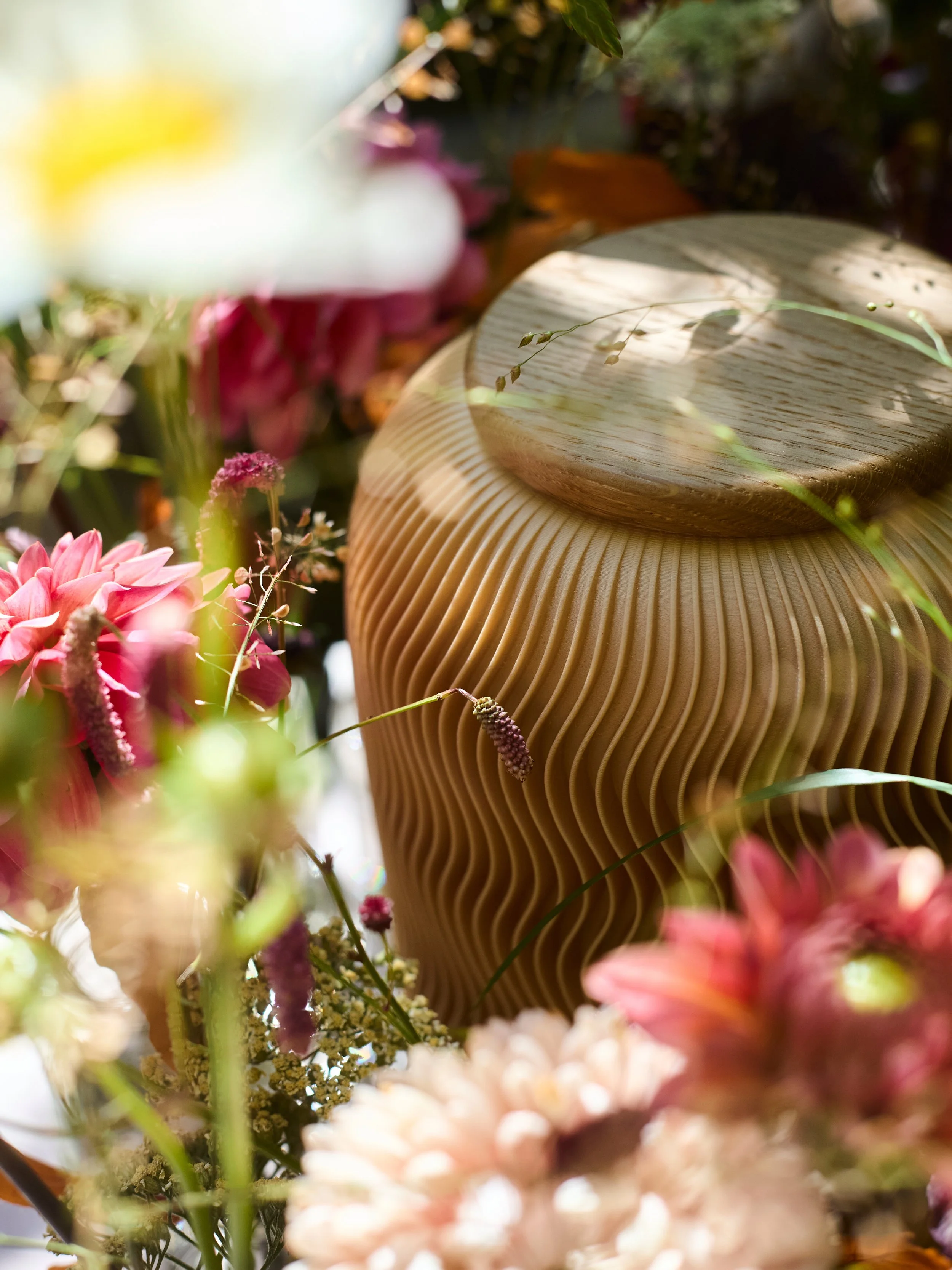 Farvel Urne Nami inmitten von bunten Blumen und Pflanzen.