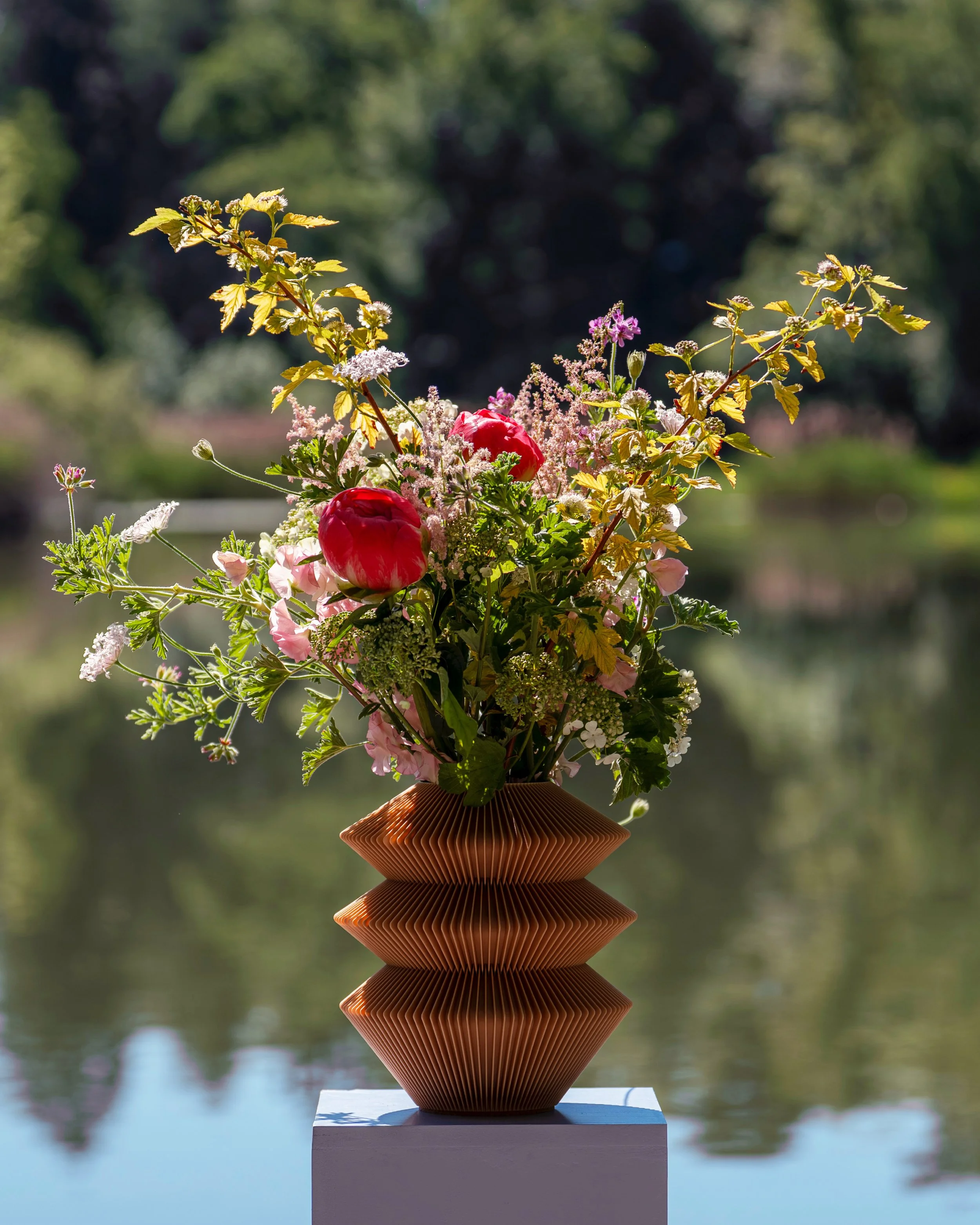 Farvel Urne mit Vaseneinsatz und frischen Blumen an einem Gewässer