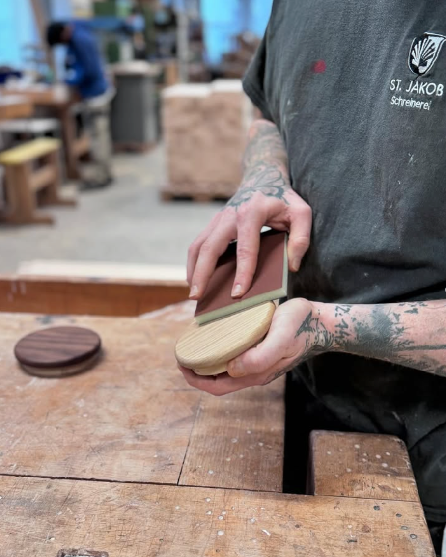 Mitarbeiter der Stiftung St. Jakob schleift einen Urnendeckel aus Holz