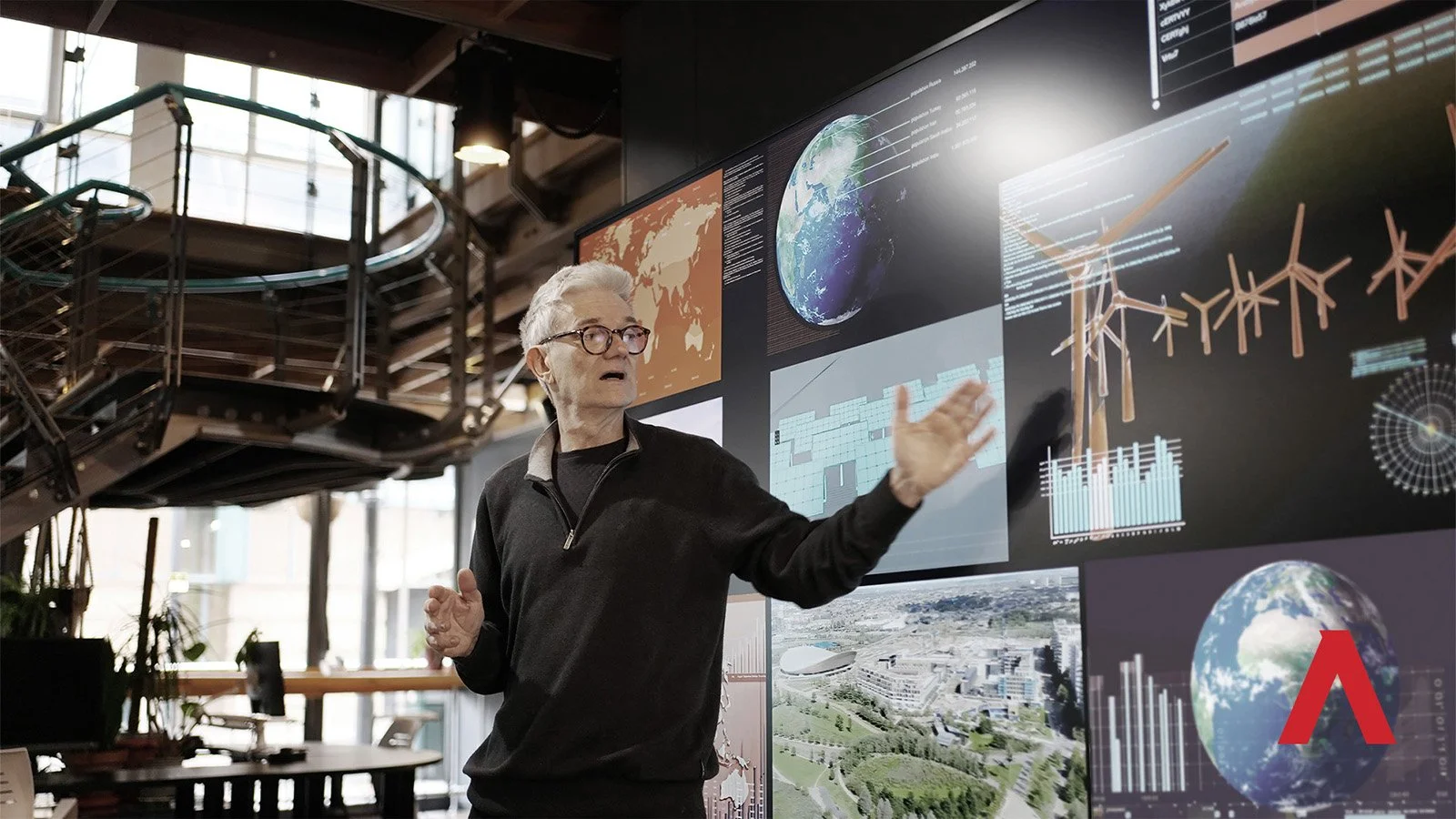 man giving a lecture beside a large screen, he's showing images of sustainable energy