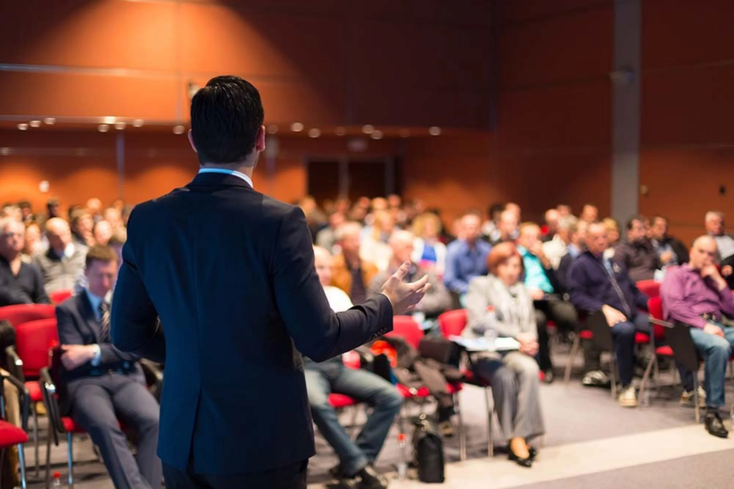A business man standing in front of a large group business men and women