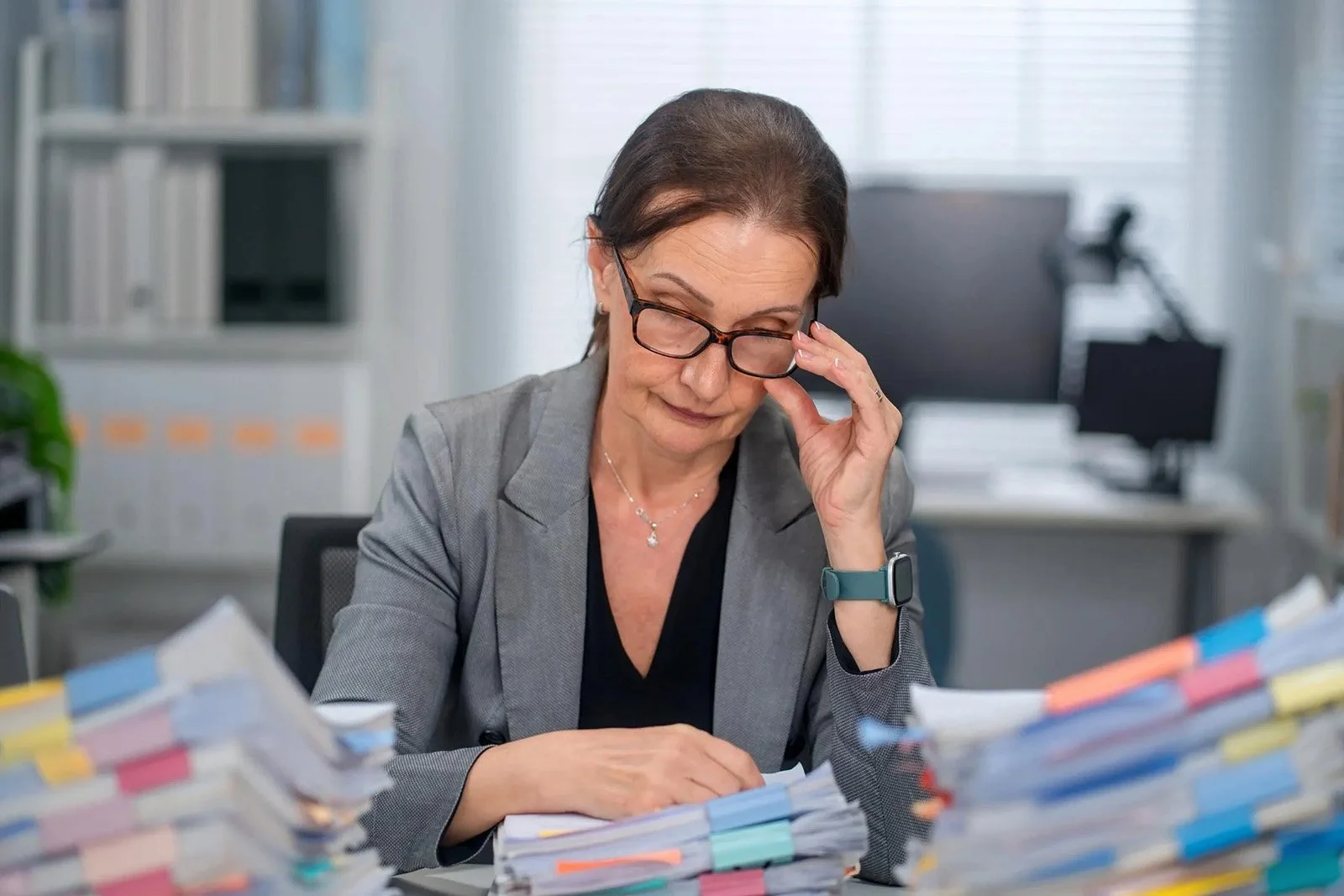 Woman with glasses looking down at large stacks of business reports
