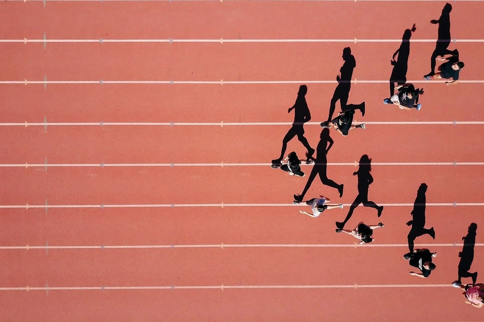 Aerial view of runners mid-race casting long shadows, empty lanes beside them at a Sports Mental Performance Counseling in St. Louis & St. Charles track event.